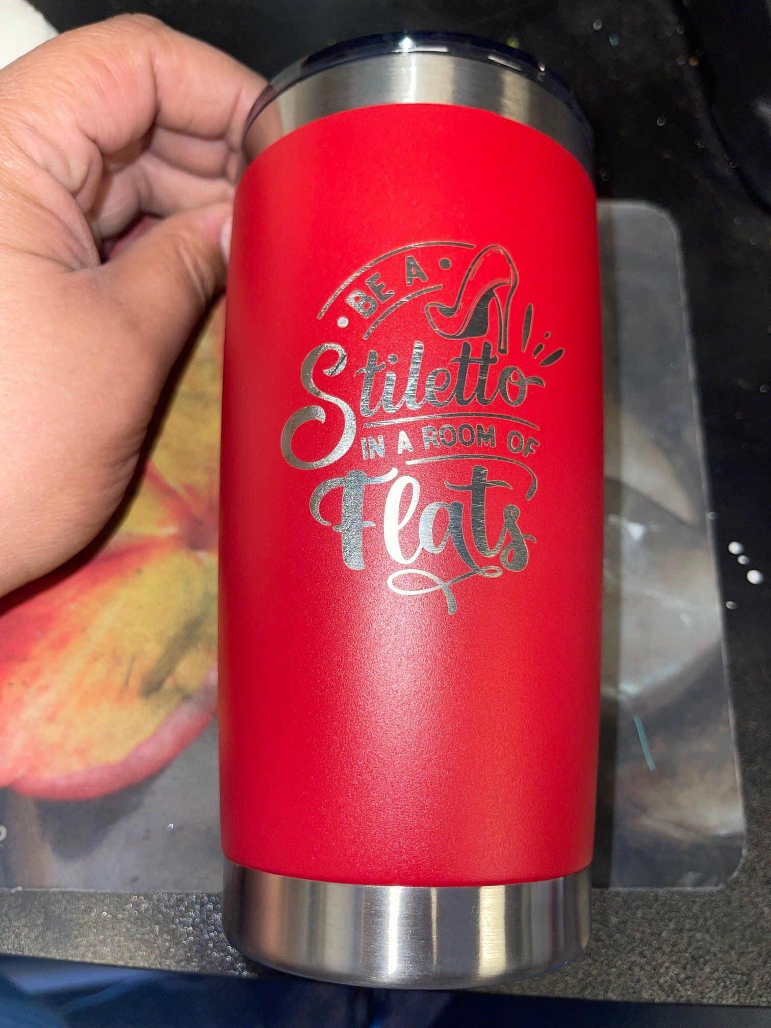A person is holding a red tumbler with a quote on it.
