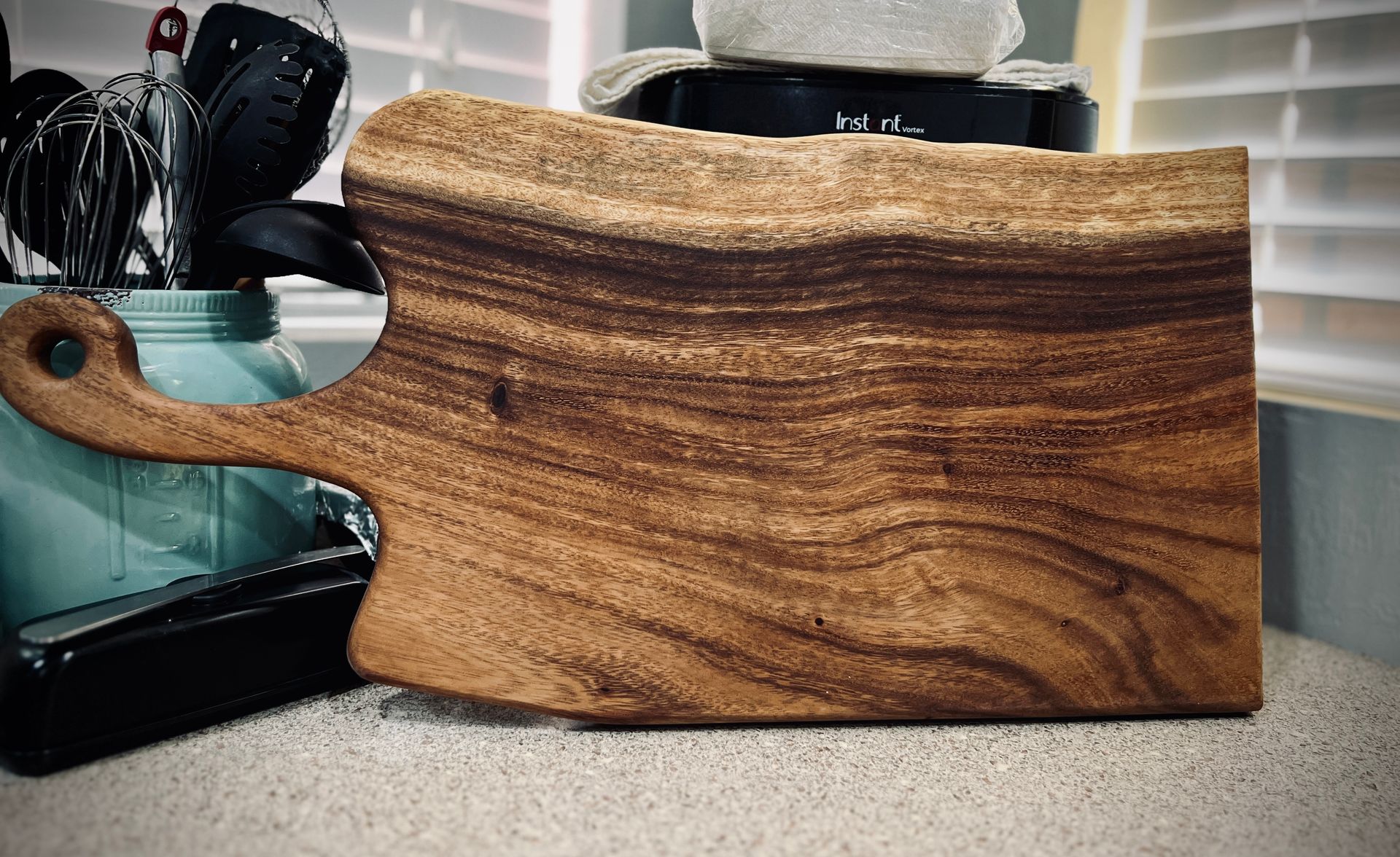 A wooden cutting board with a handle is sitting on a counter.