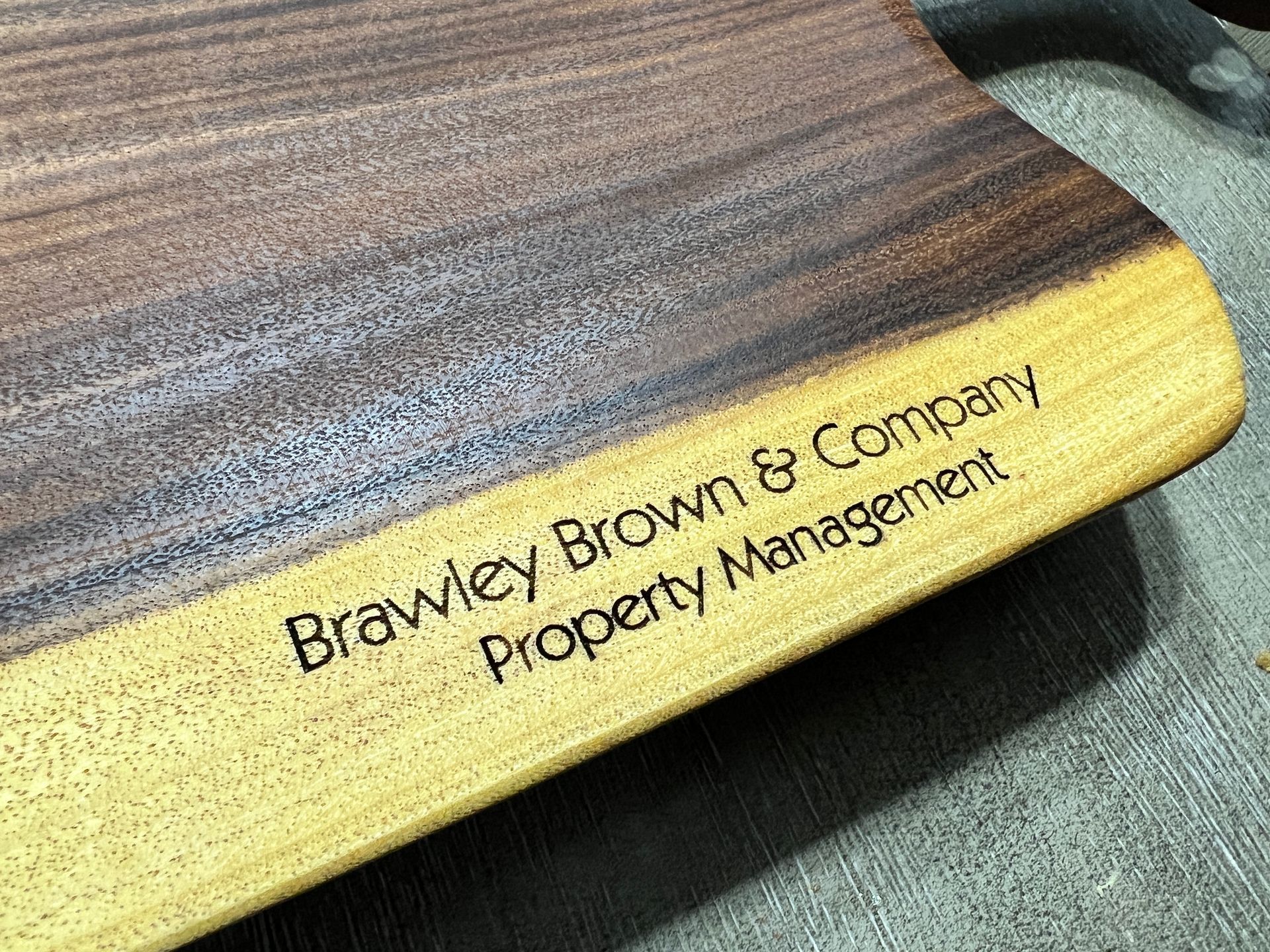 A wooden cutting board with the words brawley brown & company property management engraved on it.