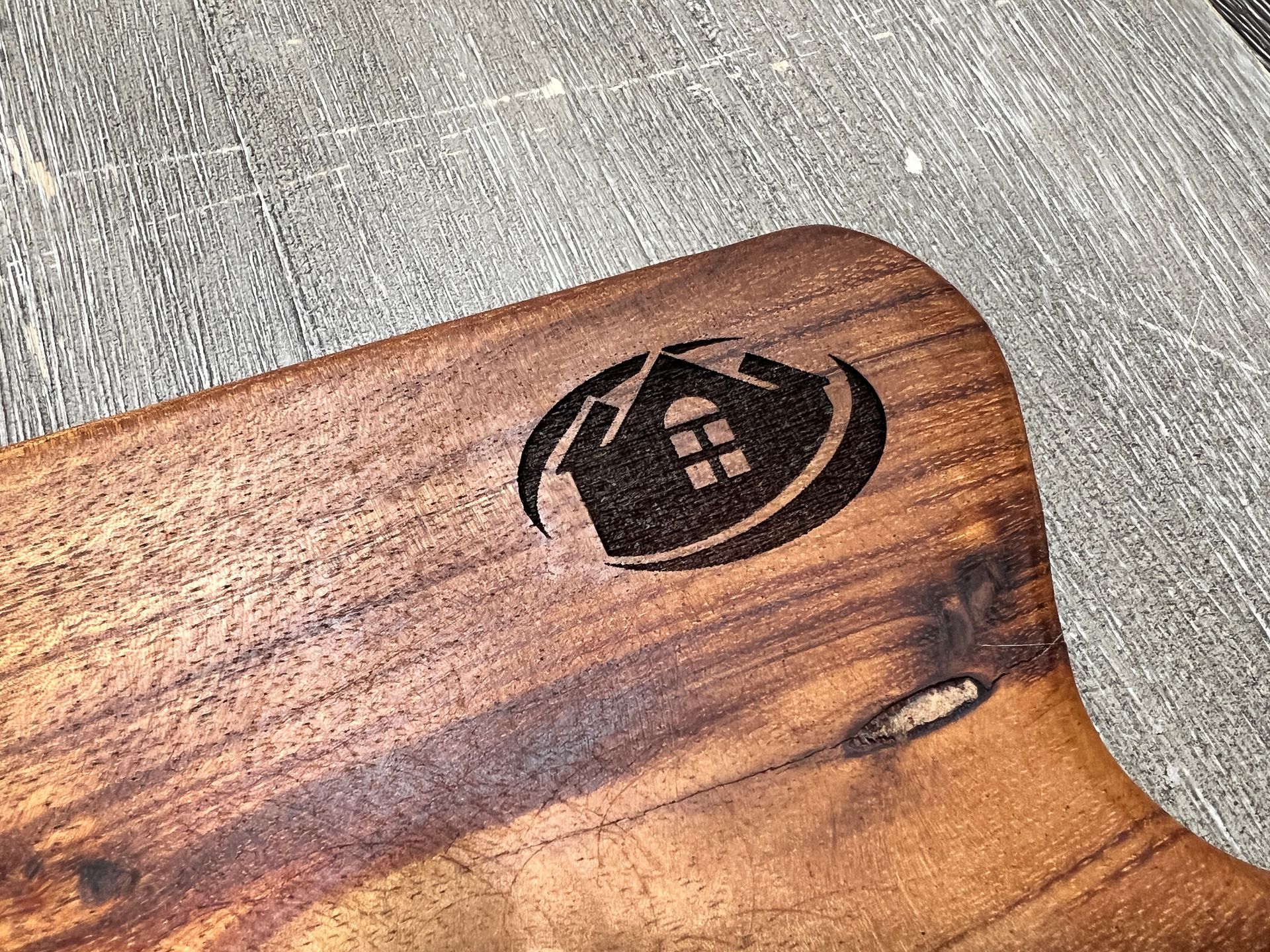 A wooden cutting board with a house logo on it.