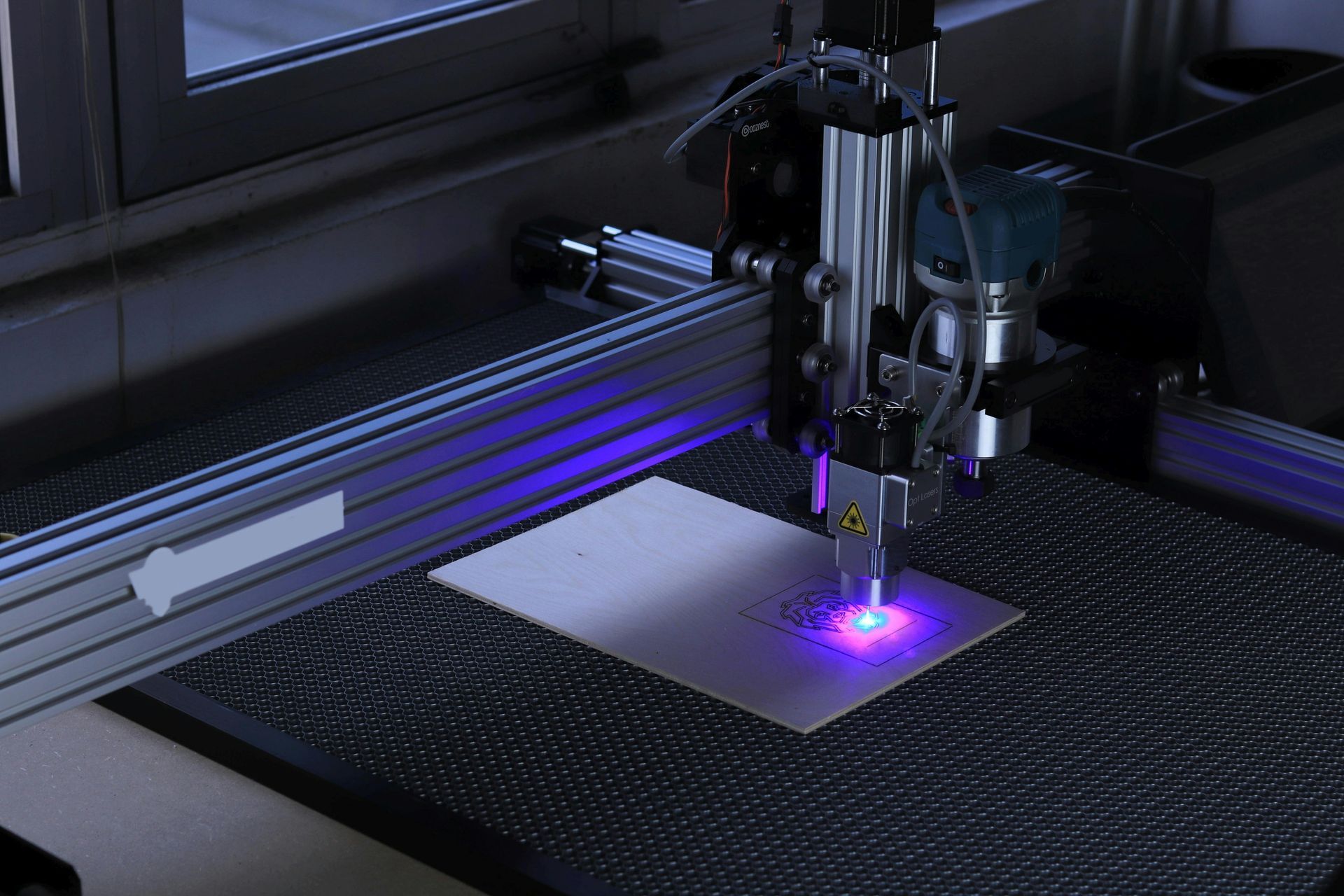 A laser engraver cutting a piece of wood with a purple light coming out of it.