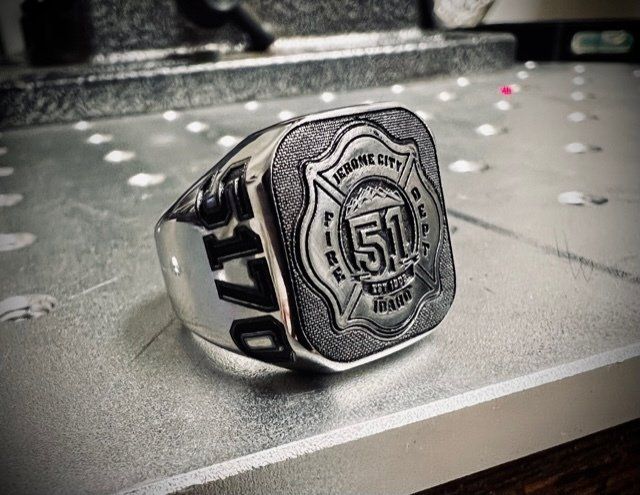 A silver ring with a fire department logo on it is sitting on a table.