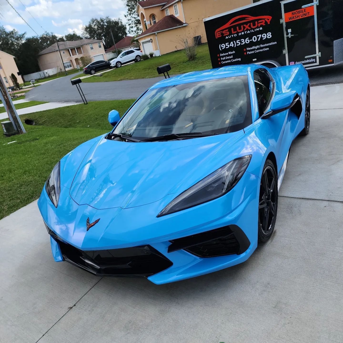 Bright blue Corvette parked on a driveway, next to a moving truck.