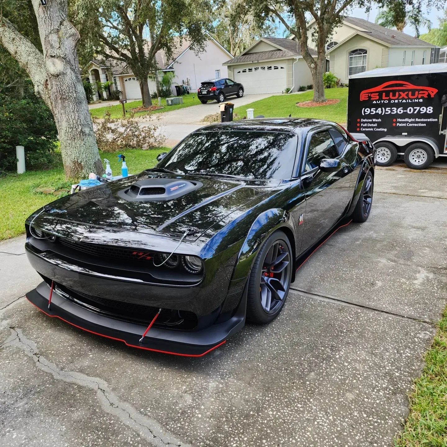 Black Dodge Challenger with red accents parked on a driveway, mobile car wash truck nearby.