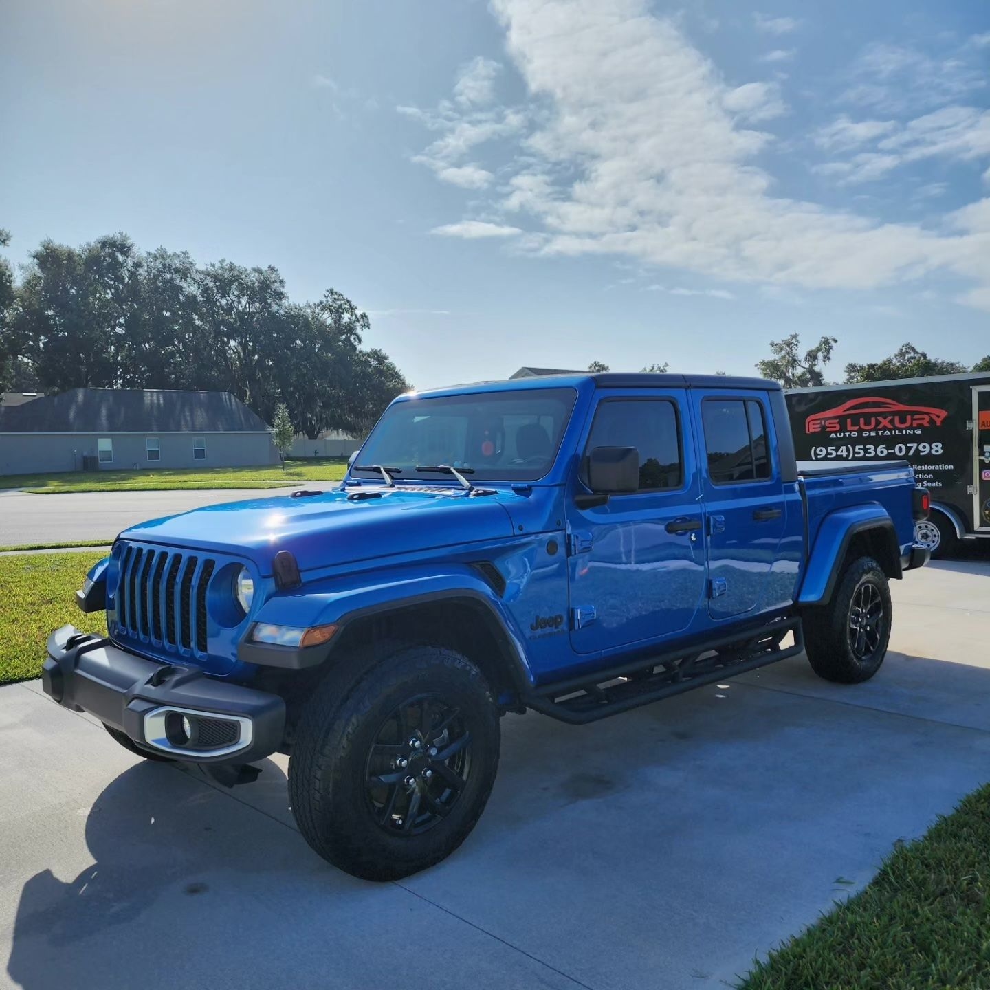 Blue Jeep Gladiator pickup truck parked on a driveway, sunny day.