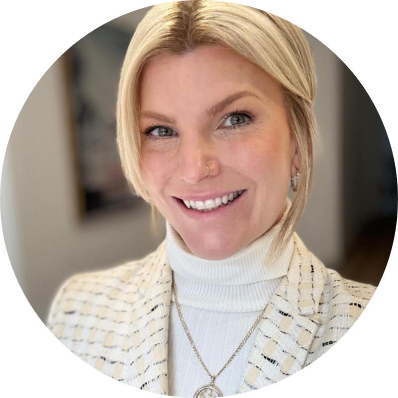 A woman wearing a white turtleneck and a white jacket smiles for the camera