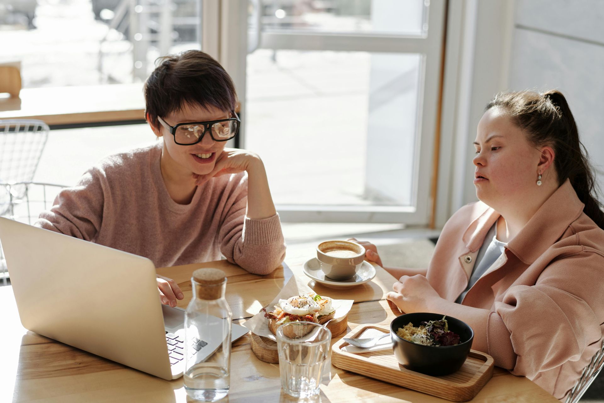 Two women are sitting at a table with a laptop and drinking coffee.