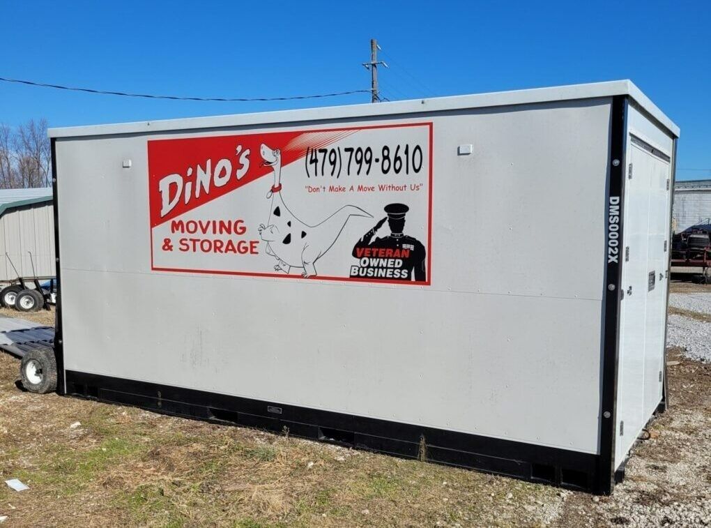 White storage container with Dino's Moving & Storage logo, phone number, and a graphic of a soldier, outdoors on gravel.
