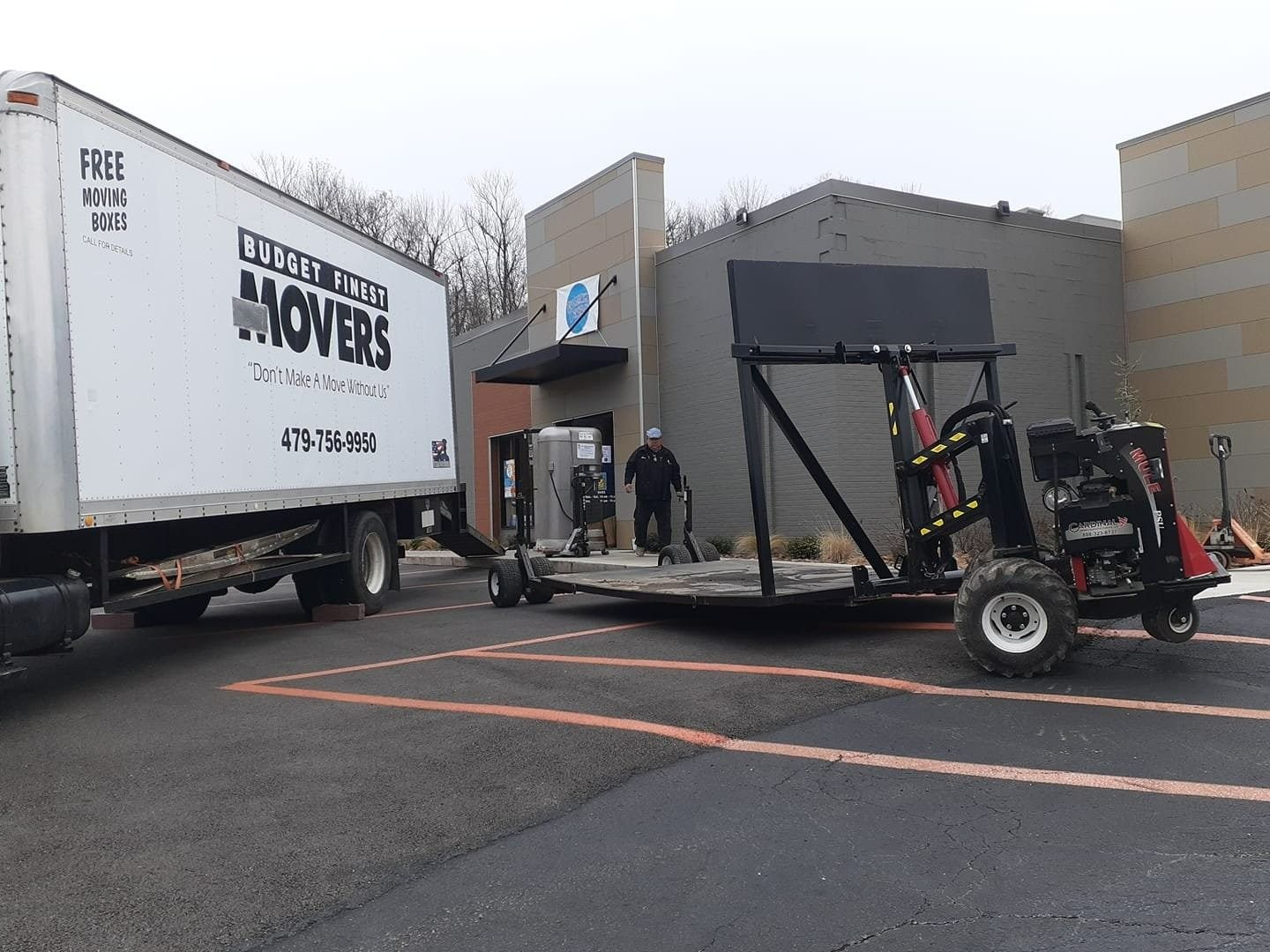 Movers loading a large, upright piece of equipment from a building entrance onto a specialized hydraulic trailer.