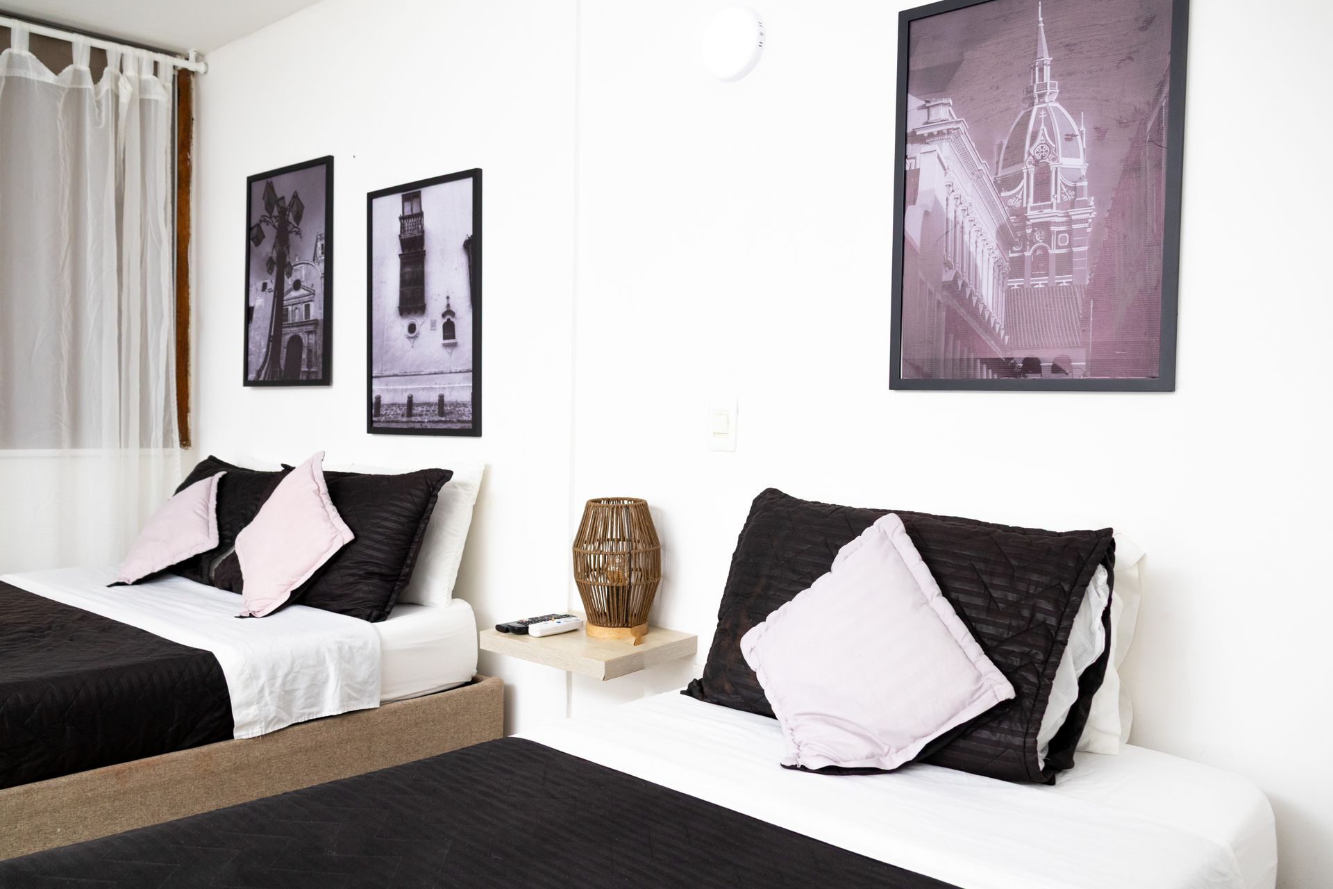 Two beds in a white room with art prints. Black and pink pillows on white bedding.