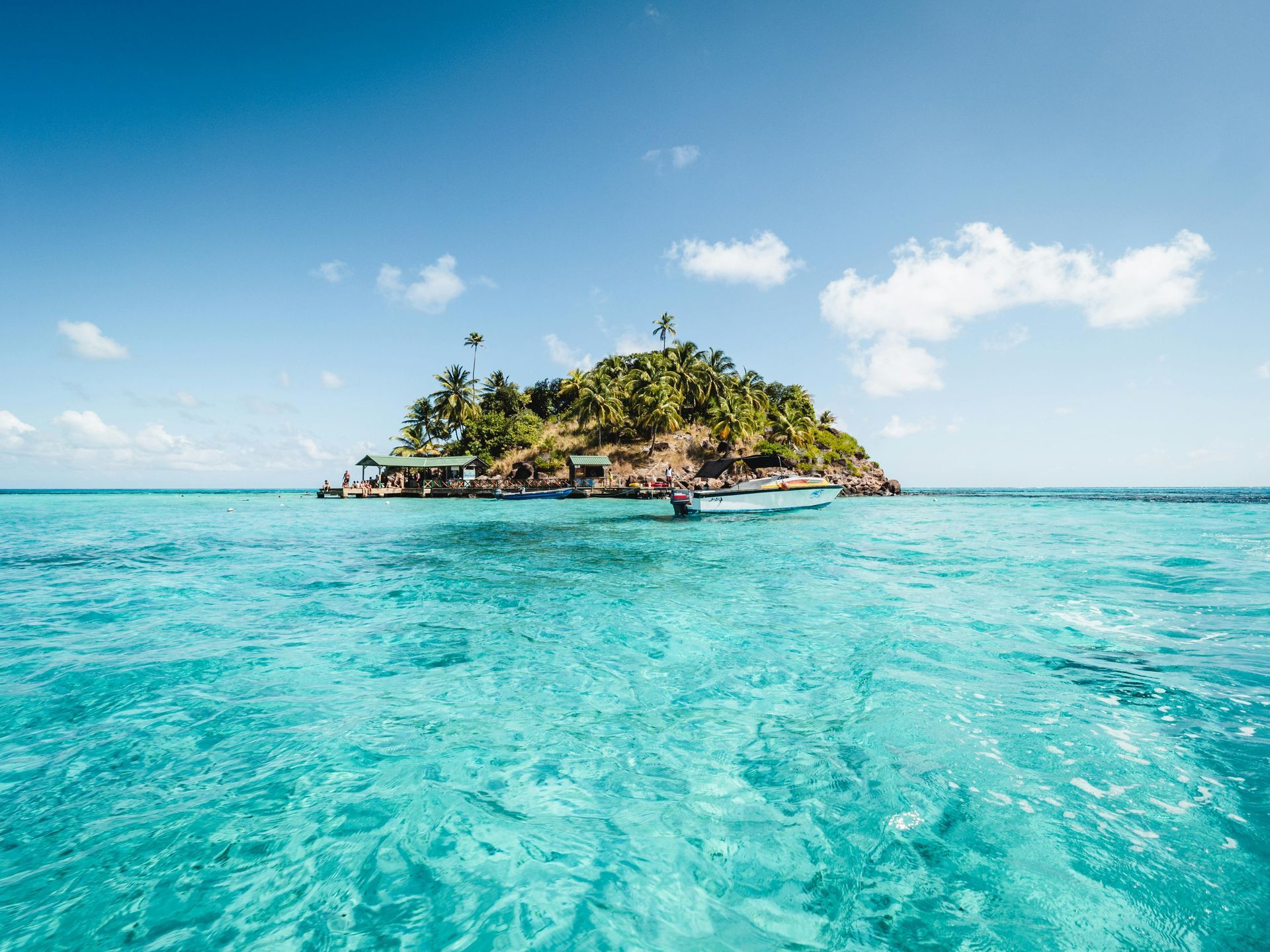 Small tropical island in turquoise water, under a blue sky with clouds. Boat docked near shore.