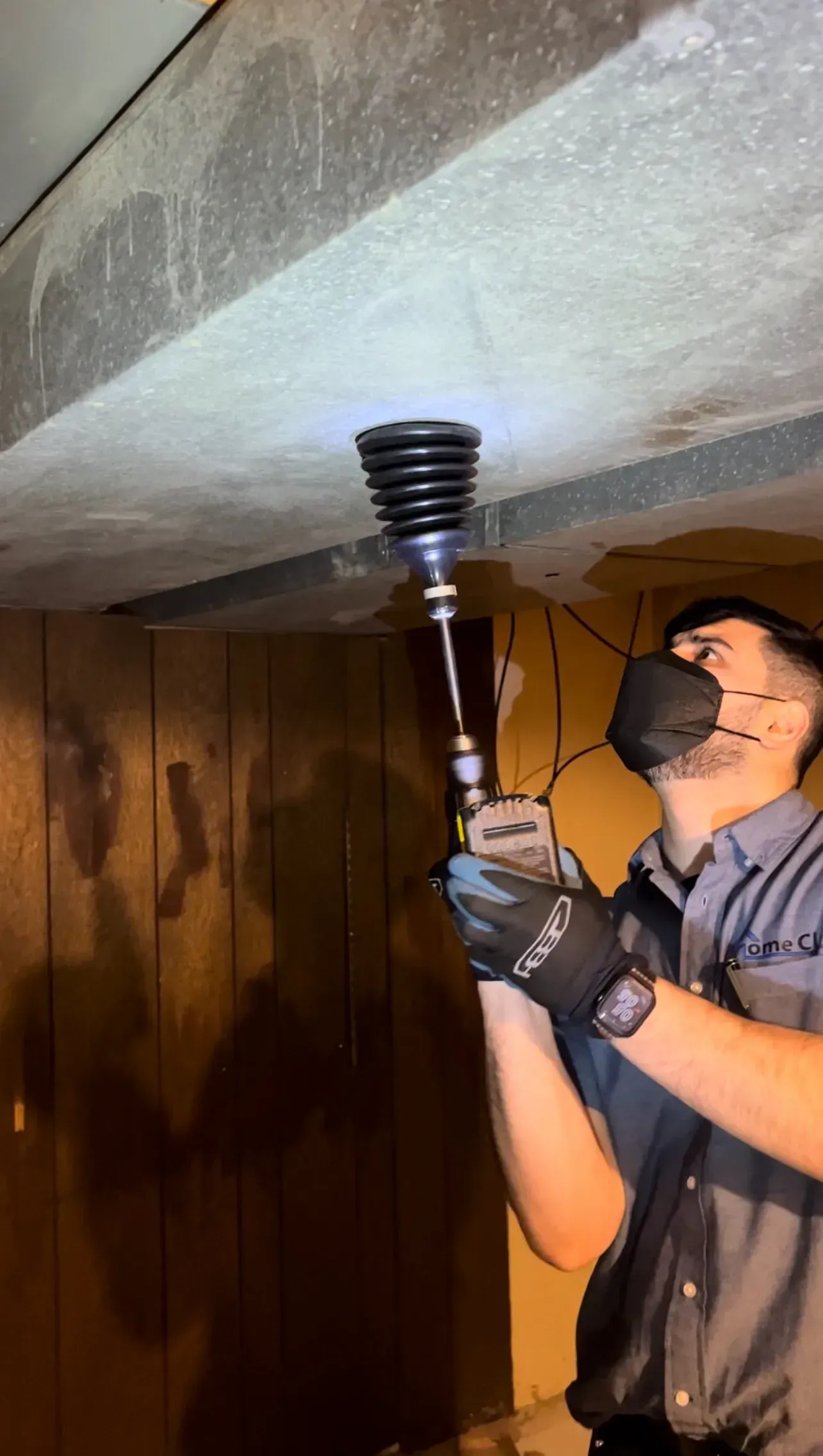 A man is holding a flashlight and a drill in a dark room.