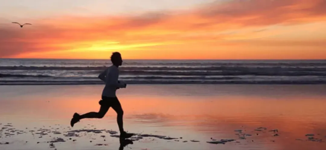 A woman is running on the beach at sunset.