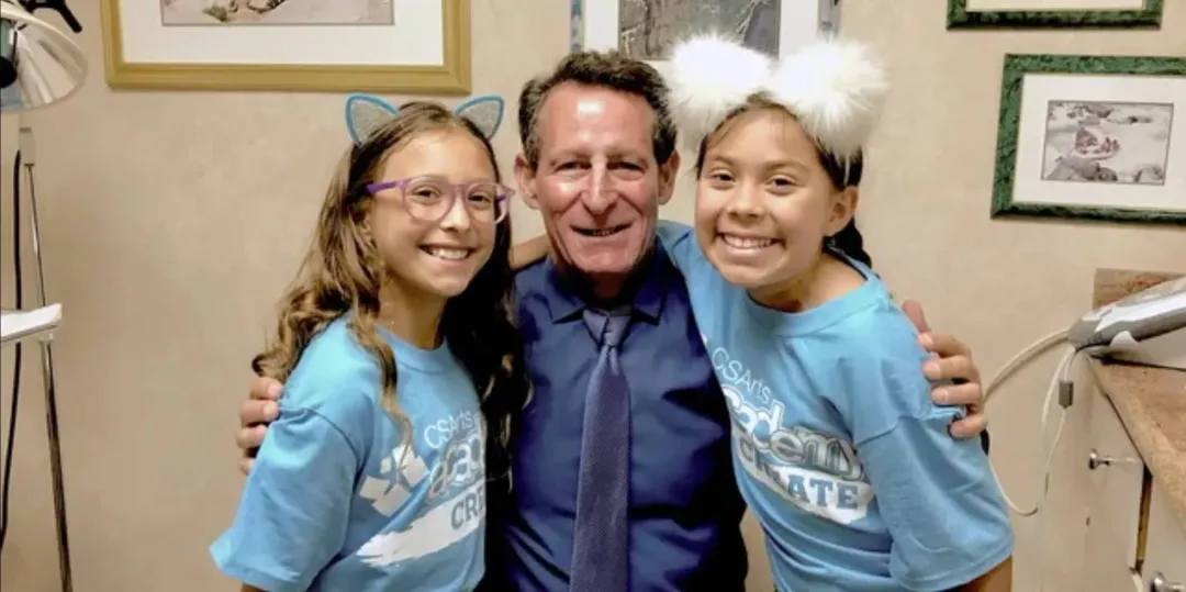 A man and two girls are posing for a picture in a dental office.