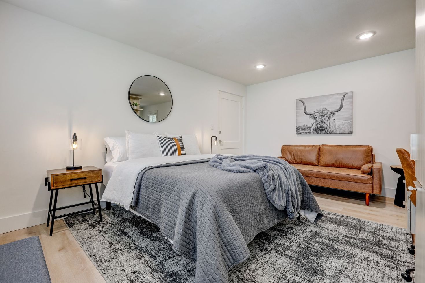 Bedroom with bed, sofa, rug, and artwork. White walls, light wood floors, neutral color scheme.