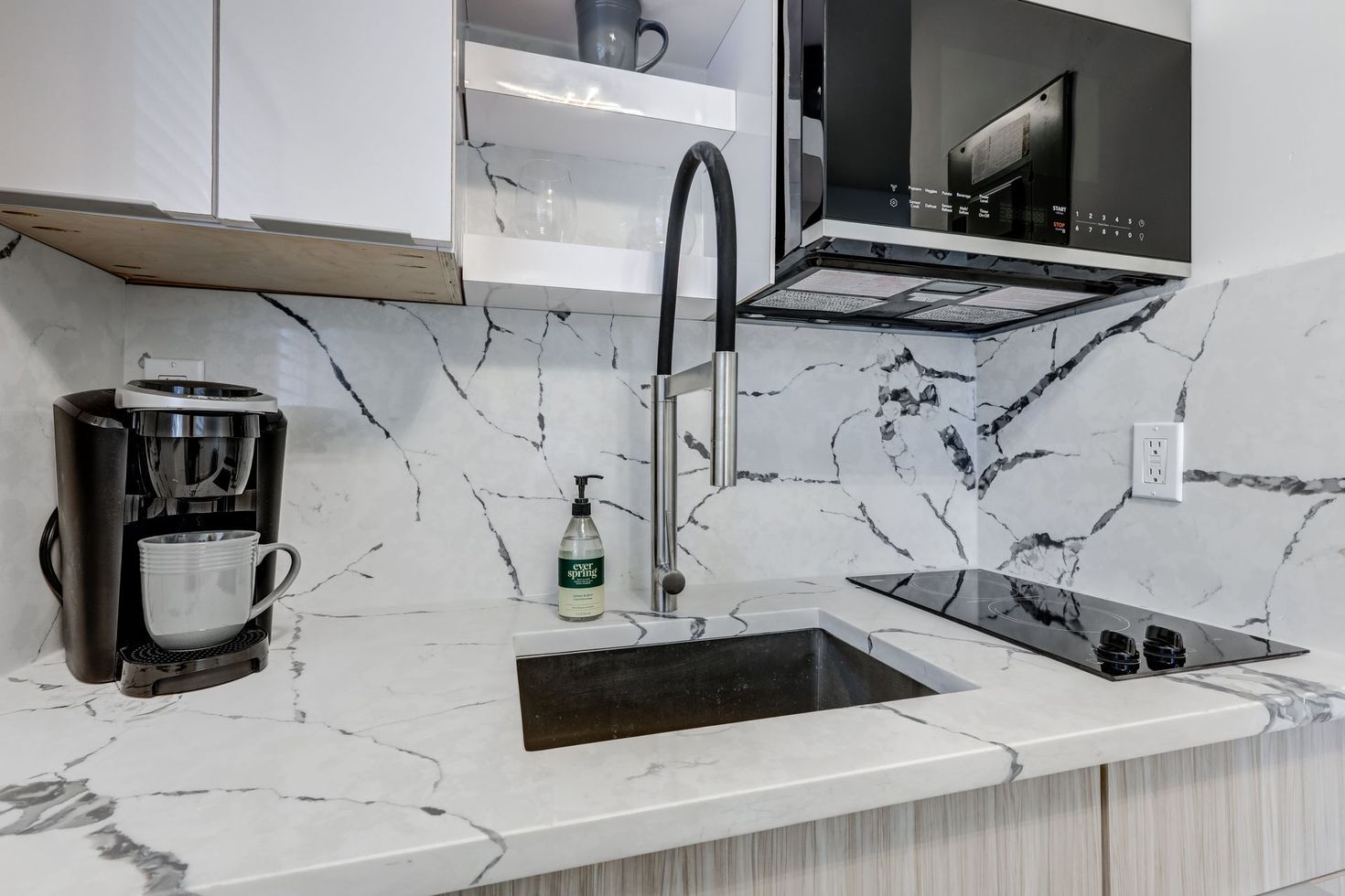 Small kitchen with white marble countertops, sink, and stovetop. Coffee maker and faucet are visible.