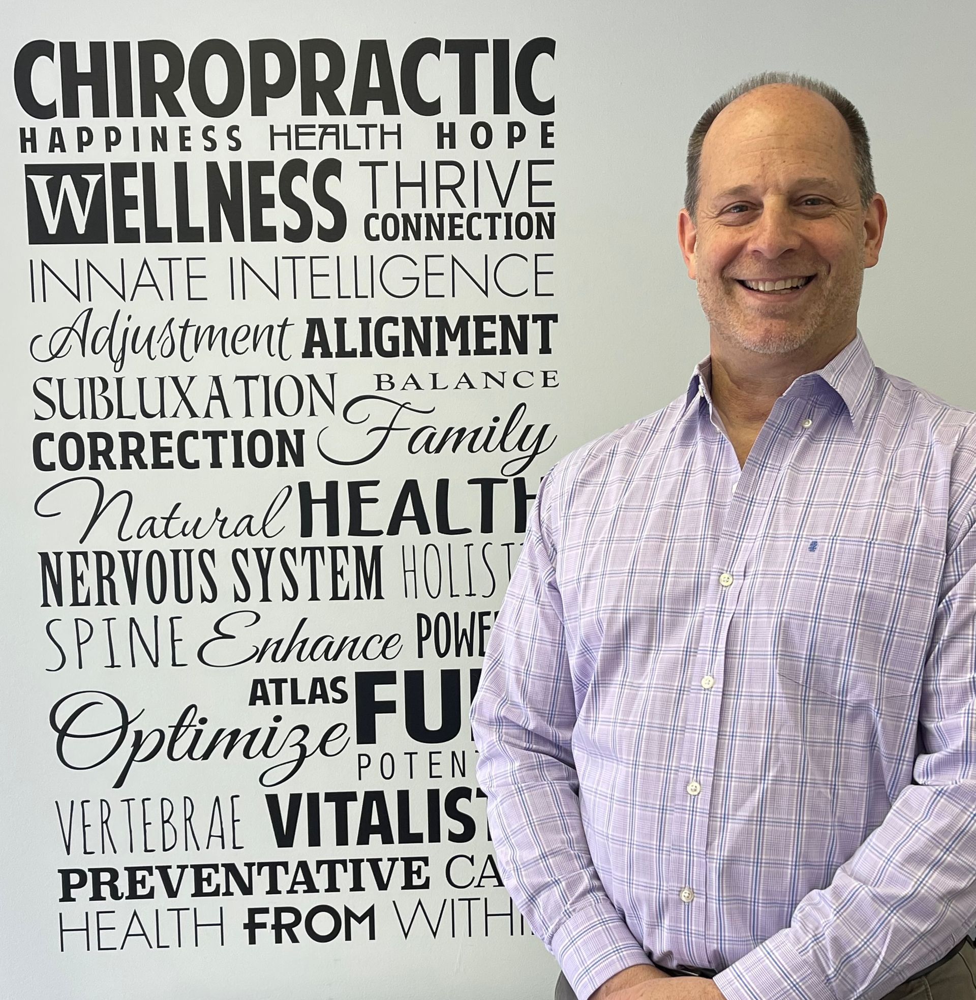 Man smiling next to a wall with chiropractic-related words like
