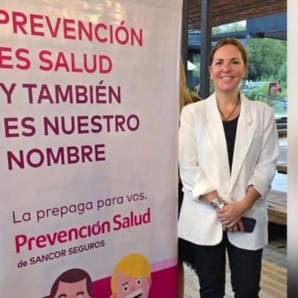 A woman stands in front of a sign that says prevencion es salud y tambien es nuestro nombre