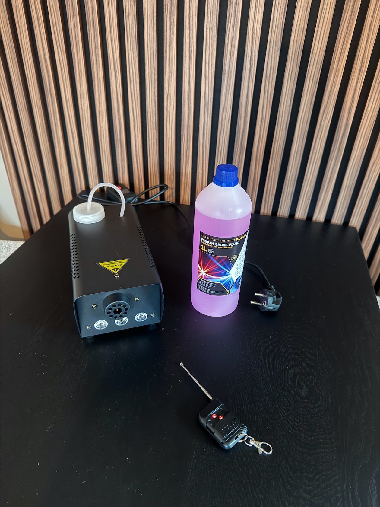 Rookmachine met vloeistoffles en afstandsbediening op een zwarte tafel.