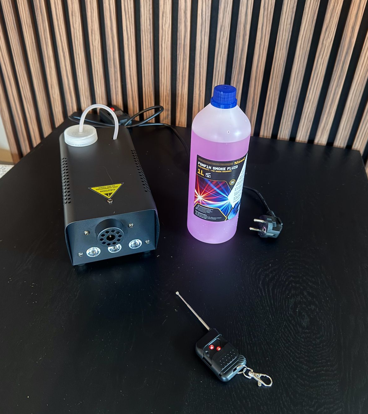 Rookmachine met vloeistoffles en afstandsbediening op een zwarte tafel.