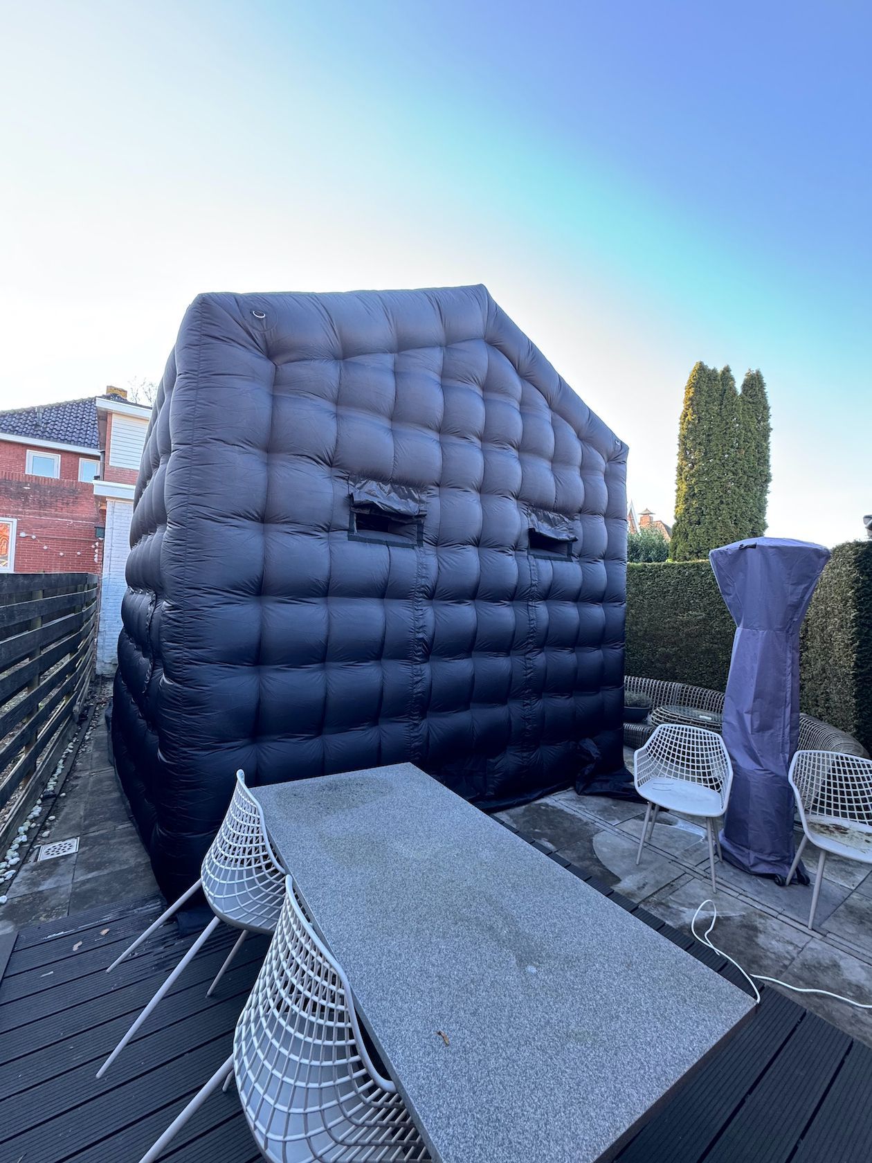 Zwarte opblaasbare kubusstructuur op een terras met een tafel en stoelen.
