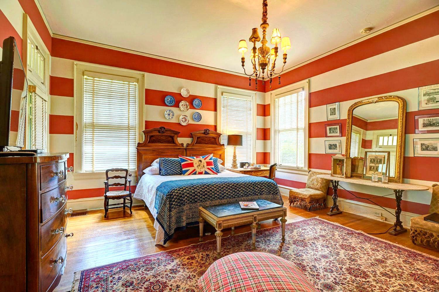 Bedroom with red and white striped walls, a bed with a blue patterned blanket, and antique furniture.