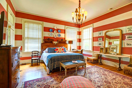 Bedroom with red and white striped walls, a bed with a blue patterned blanket, and antique furniture.