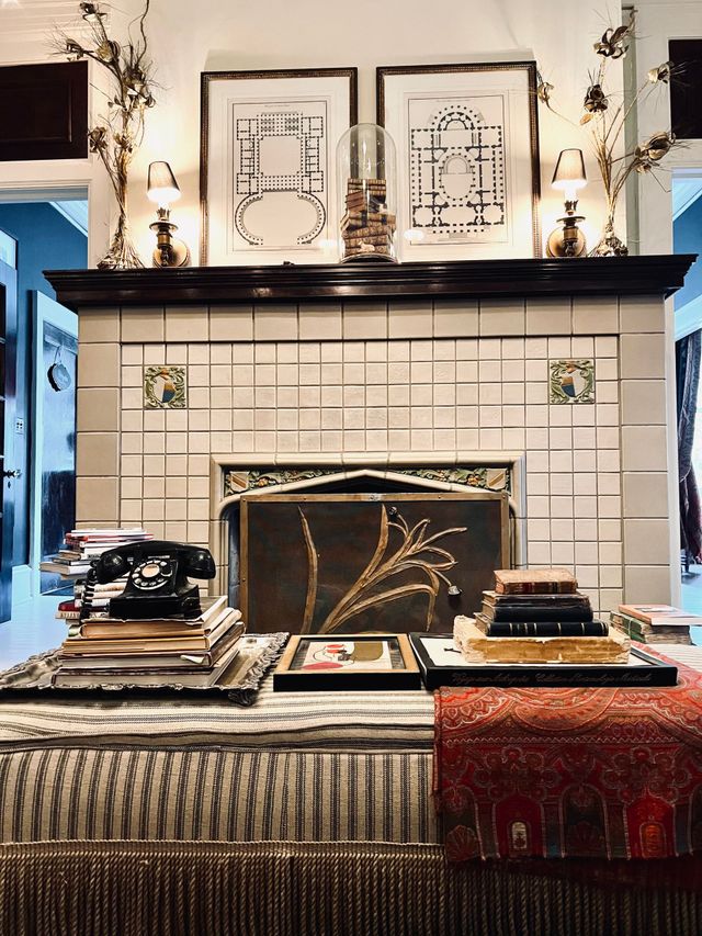 Cozy living room with fireplace, red walls, lit candles, patterned furniture, and natural light from a window.