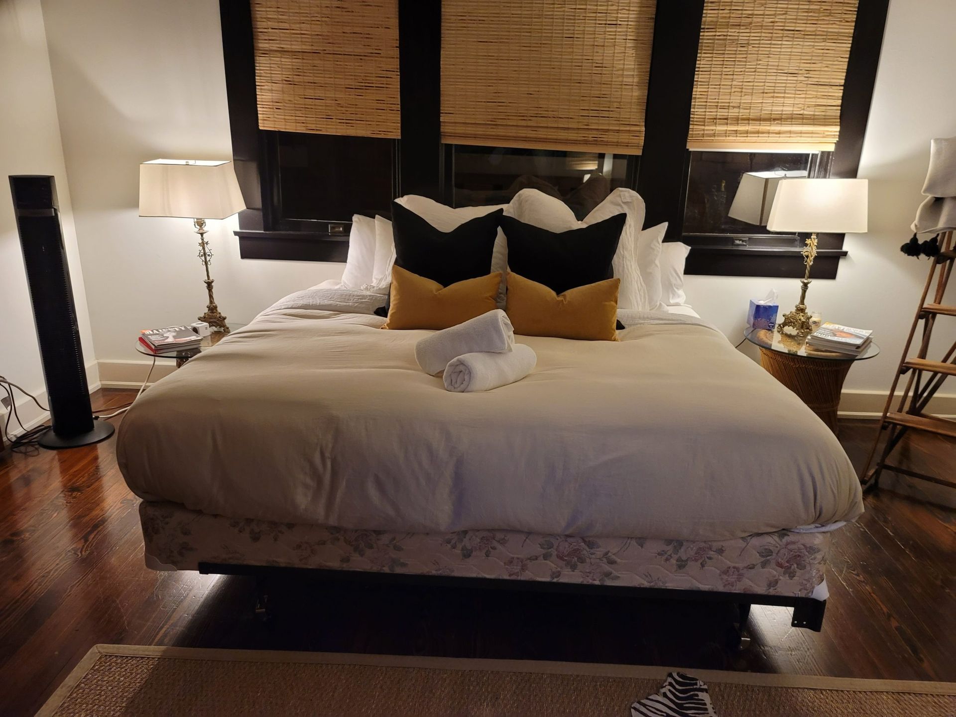 Bedroom with bed, pillows, lamps, and a wooden floor, lit by warm light.