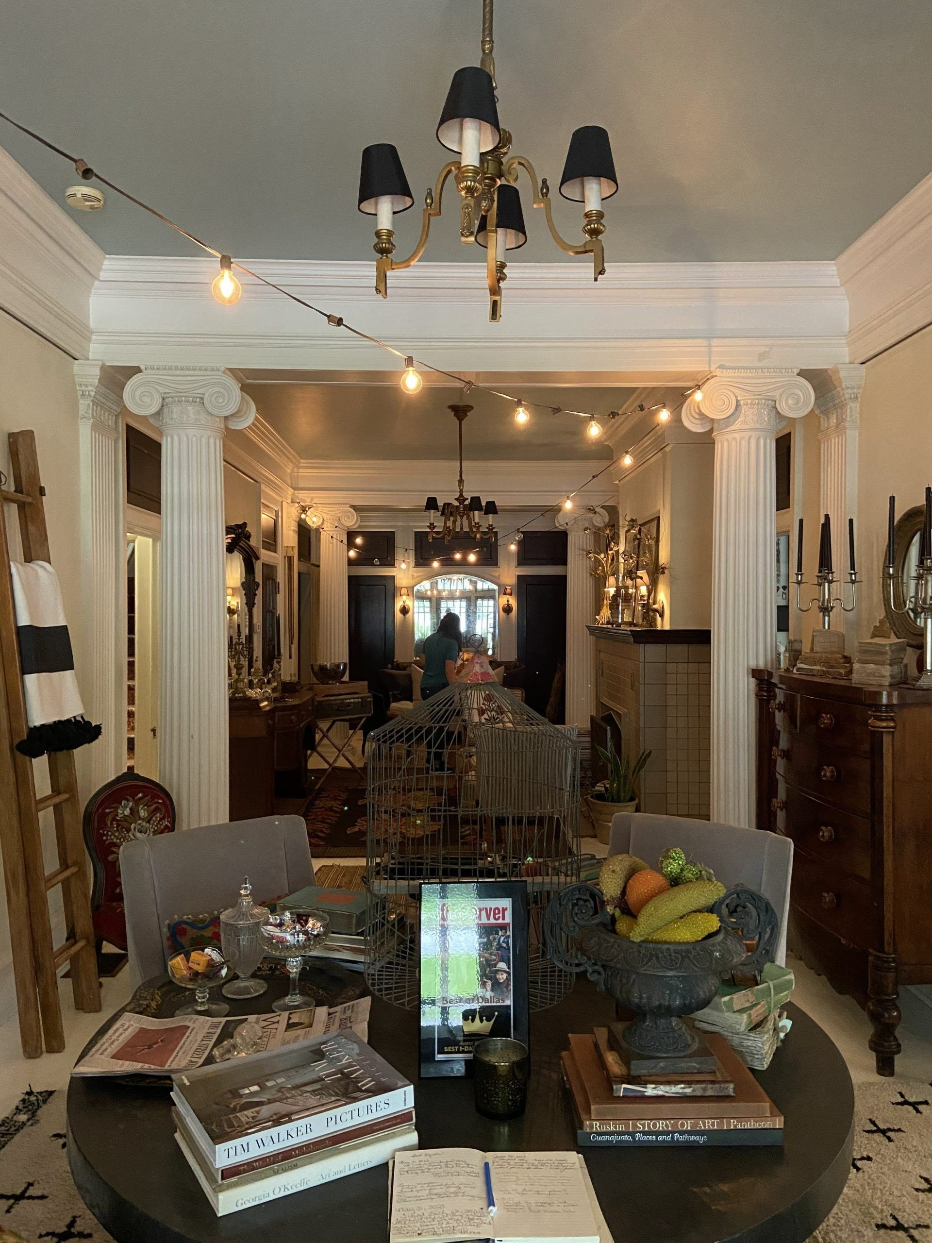 Elegant dining room with chandelier, round table, ornate decor, and a view into connected rooms.