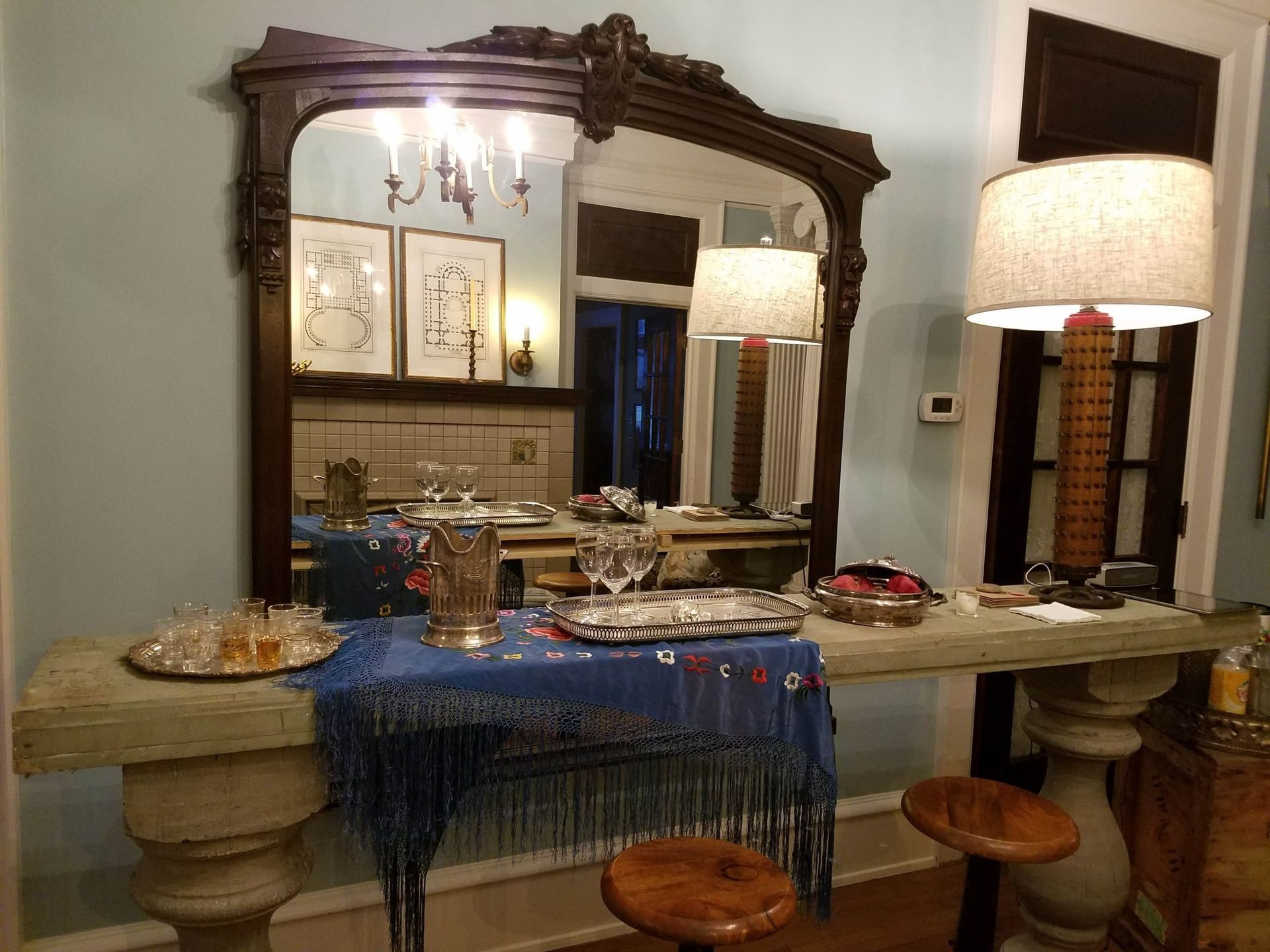Antique mirror over a table set for a party, with blue shawl, drinks, and stools.