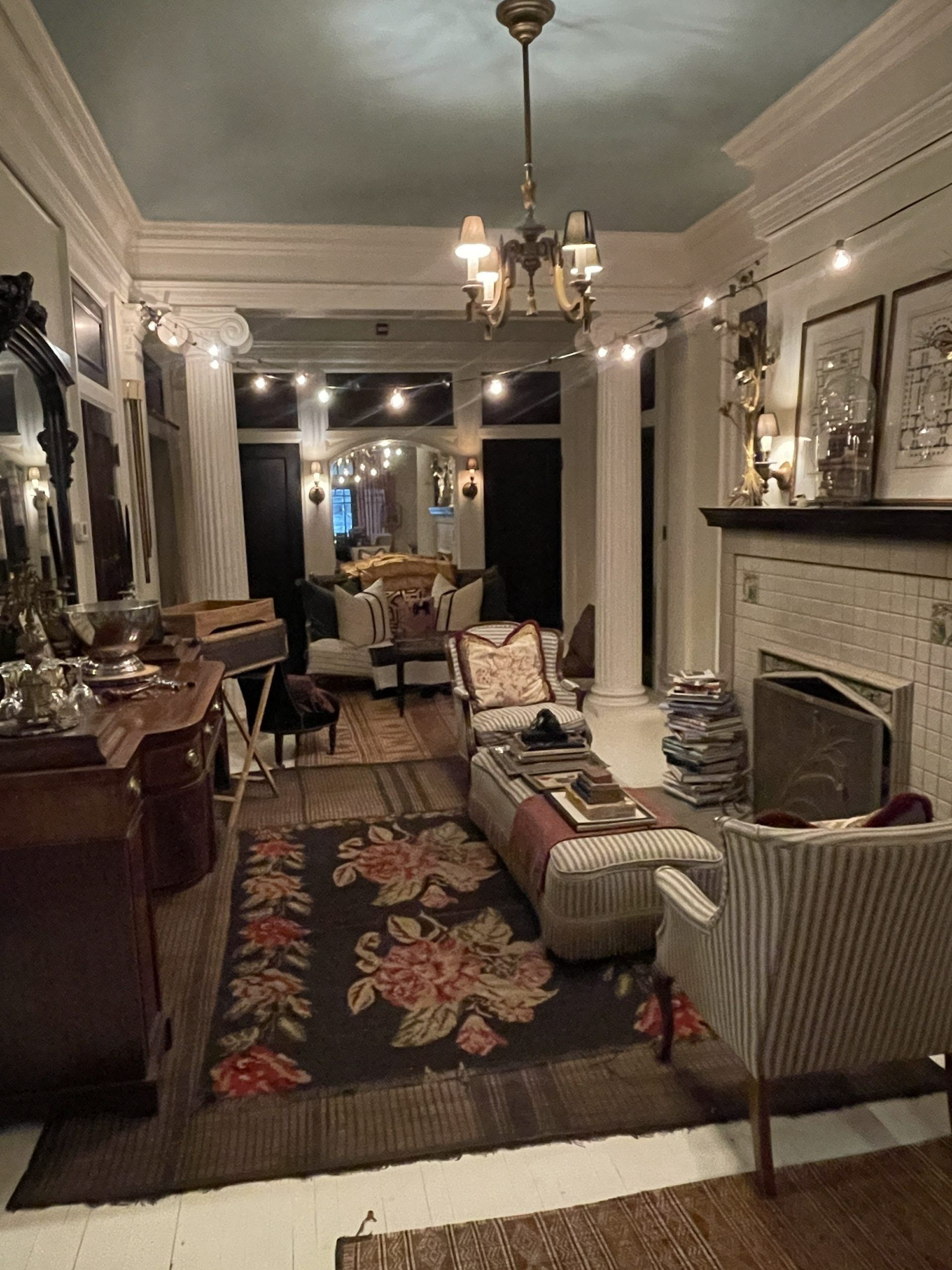 Elegant living room with floral rug, chandelier, fireplace, and various seating arrangements.