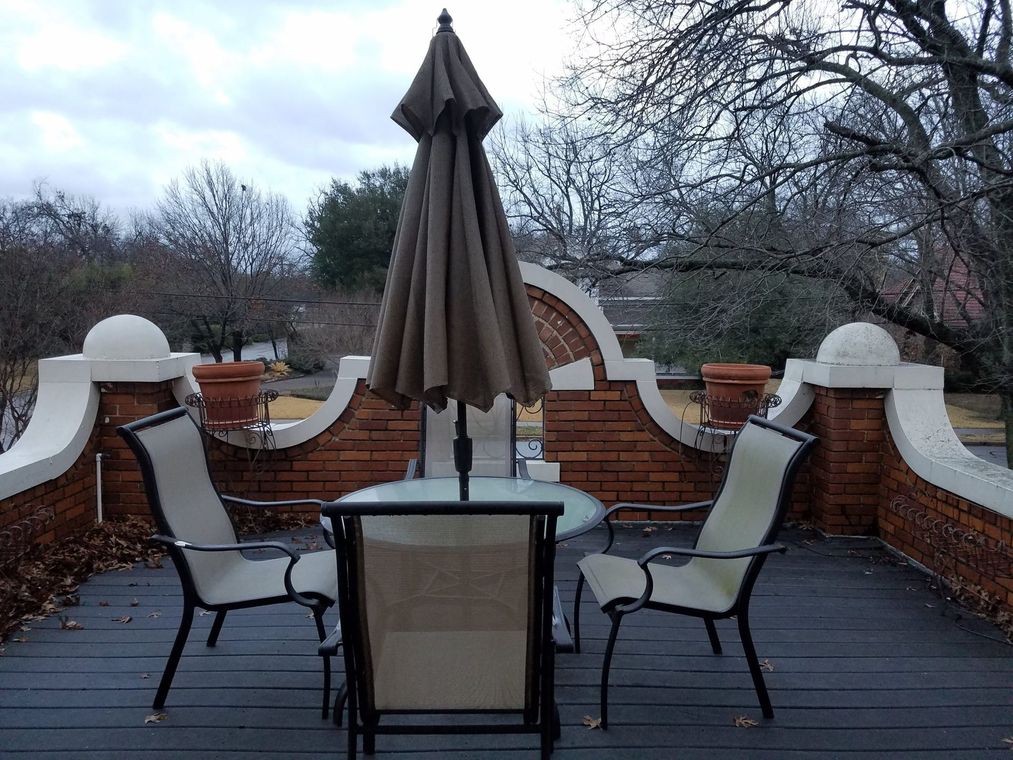 Patio with chairs, table, and closed umbrella, against a brick wall under cloudy sky.