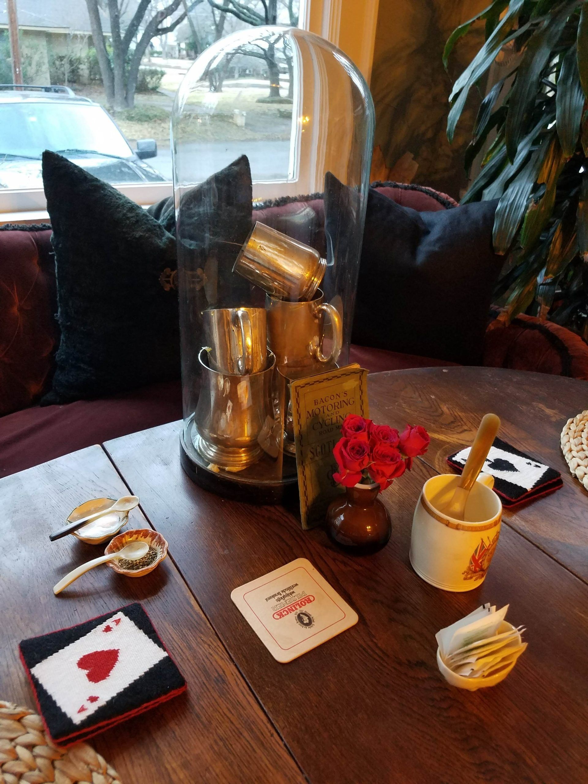 Table display: silver cups under glass dome, ace of hearts, coasters, small vase of flowers.