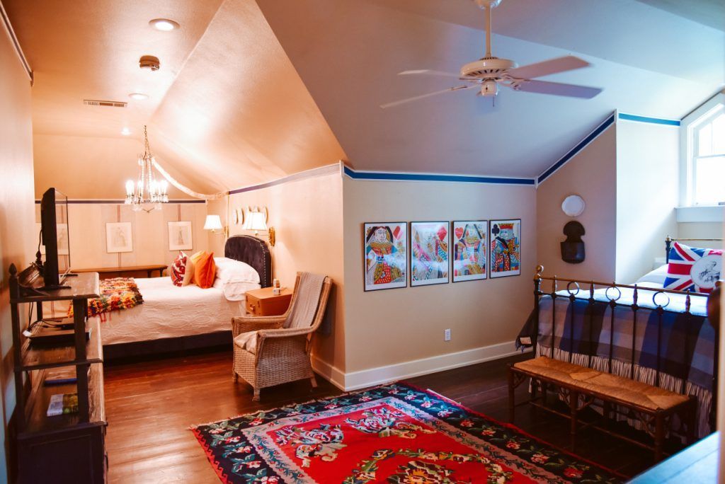 Bedroom with angled ceiling, bed, seating, rug, and artwork; warm tones.