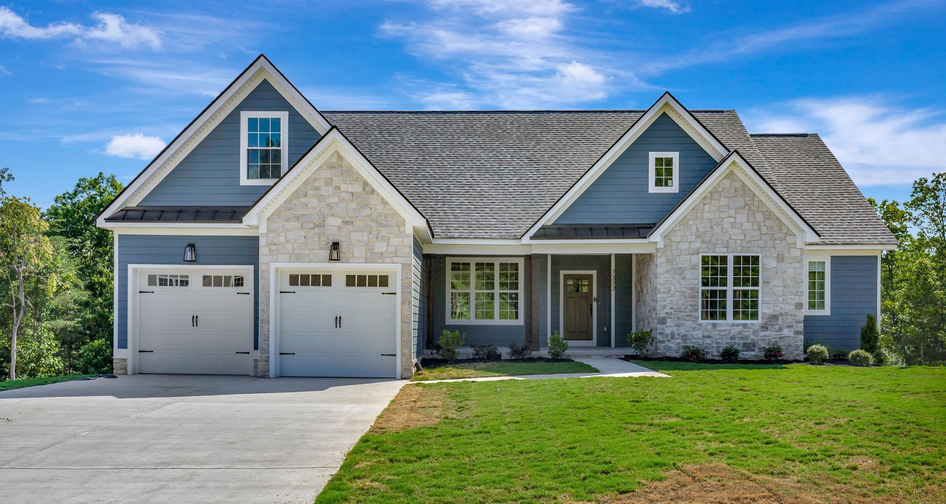A large house with a blue roof and white garage doors is sitting on top of a lush green lawn.