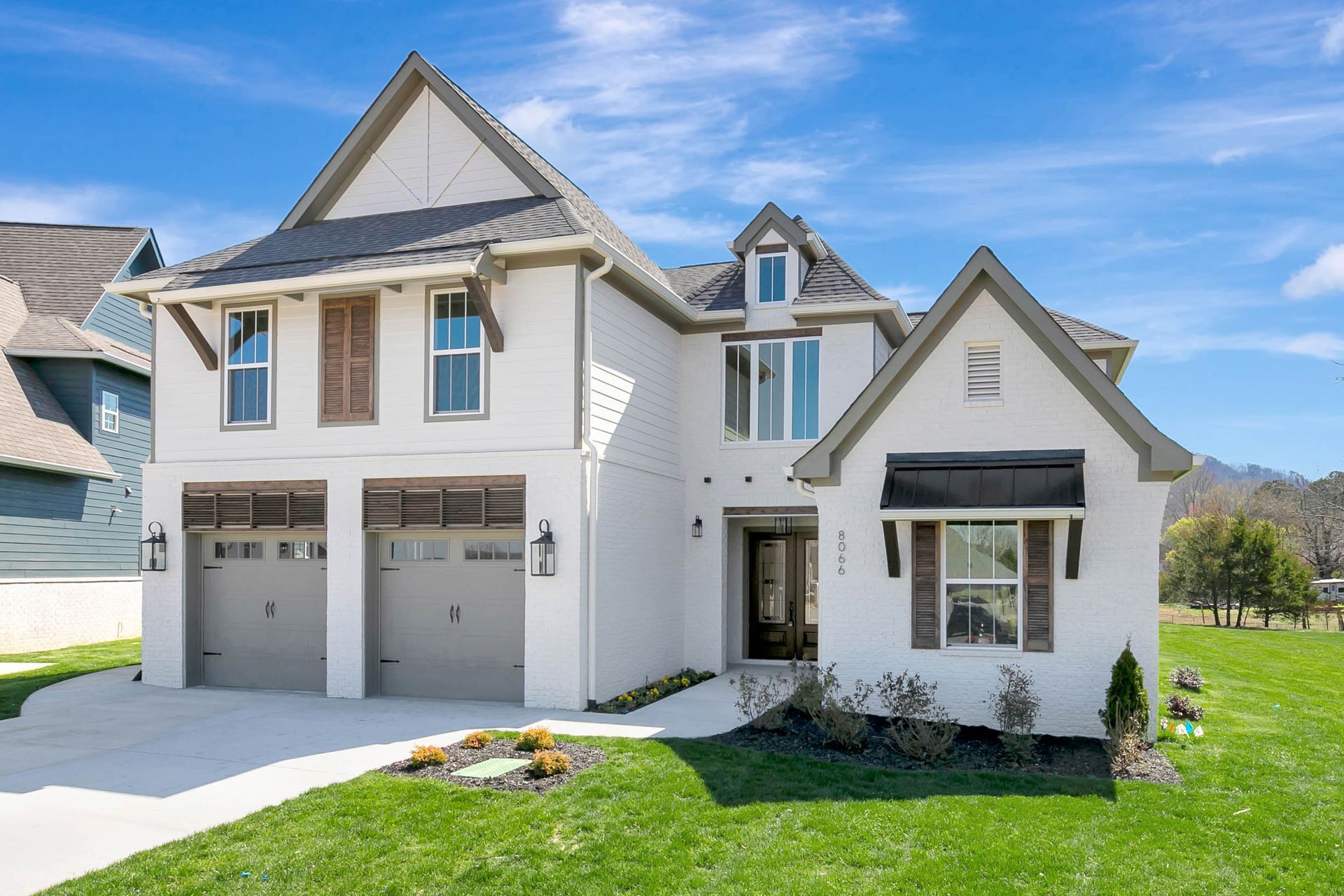 A large white house with two garages is sitting on top of a lush green lawn.