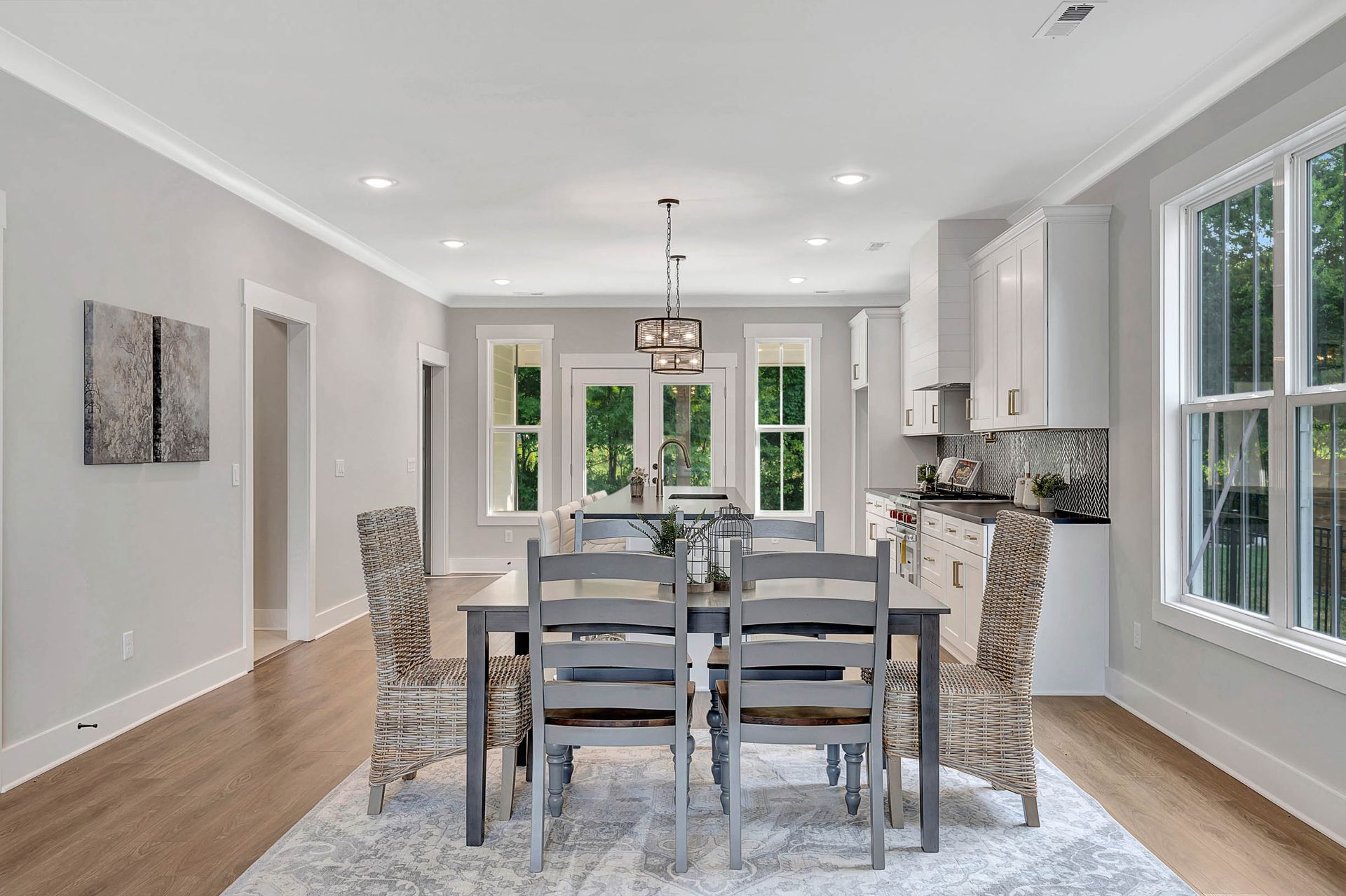 A dining room with a table and chairs and a kitchen in the background.