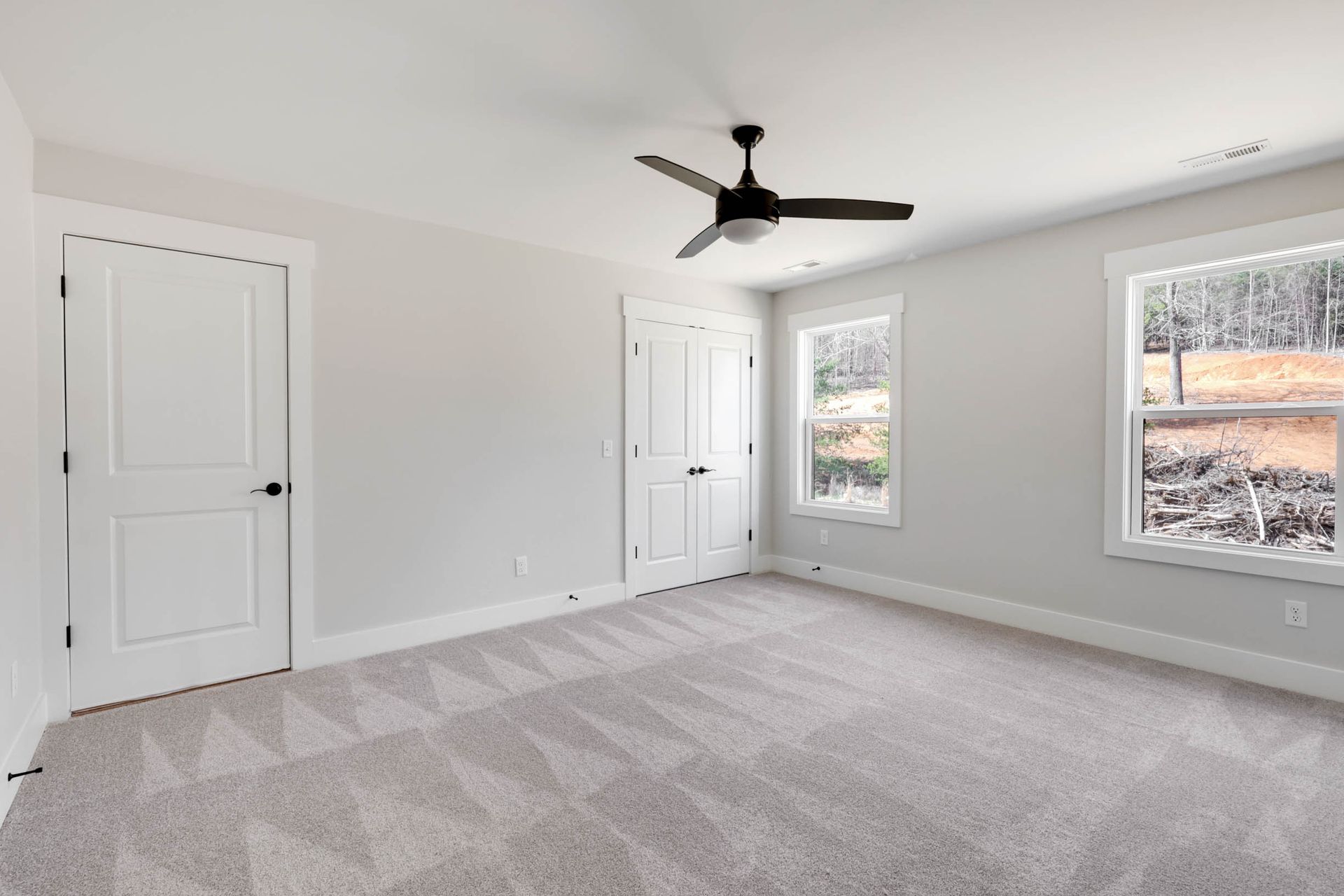 An empty bedroom with a ceiling fan and two windows.
