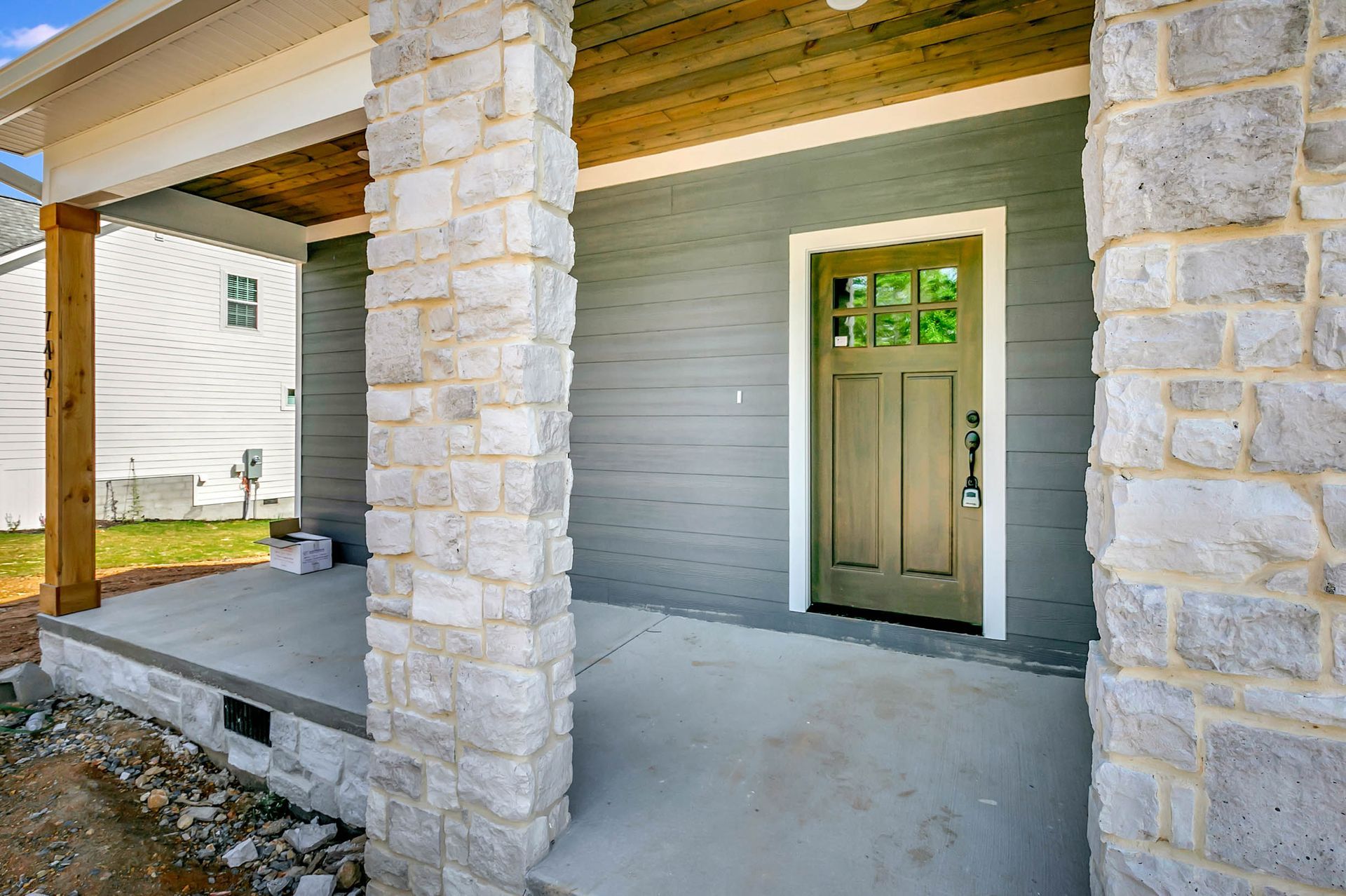 A front porch of a house with a green door and stone pillars.
