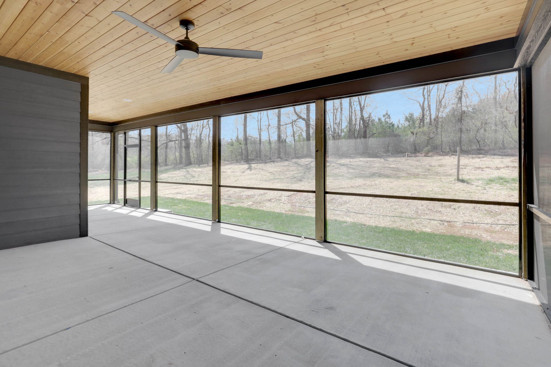 A screened in porch with a ceiling fan and a lot of windows.