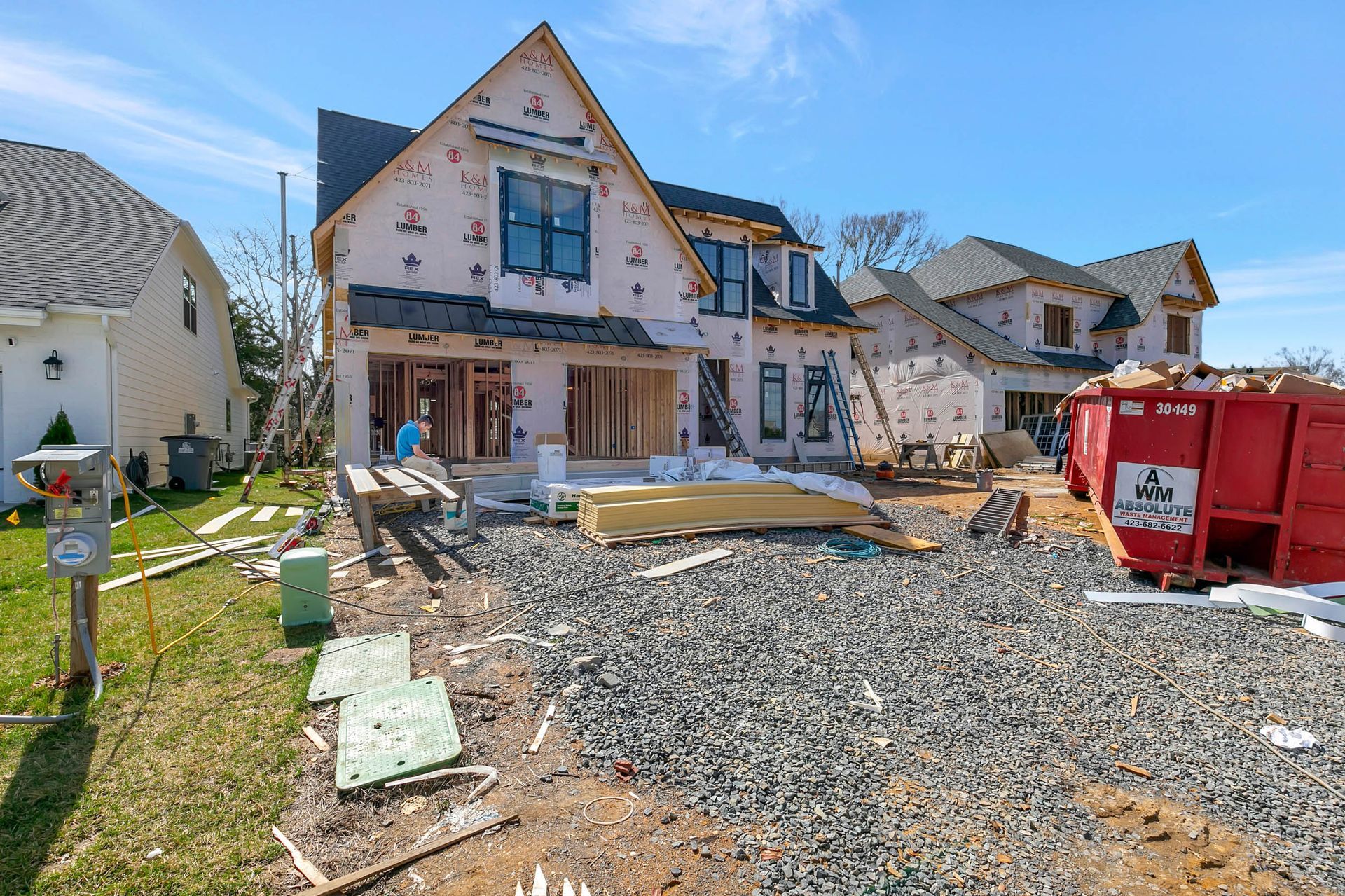 A house is being built on a gravel lot next to a dumpster.