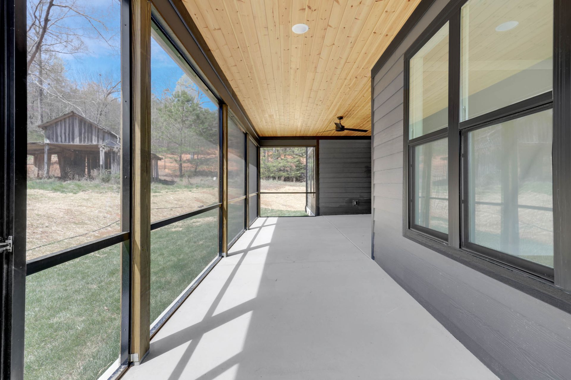 A screened in porch with a lot of windows and a wooden ceiling.