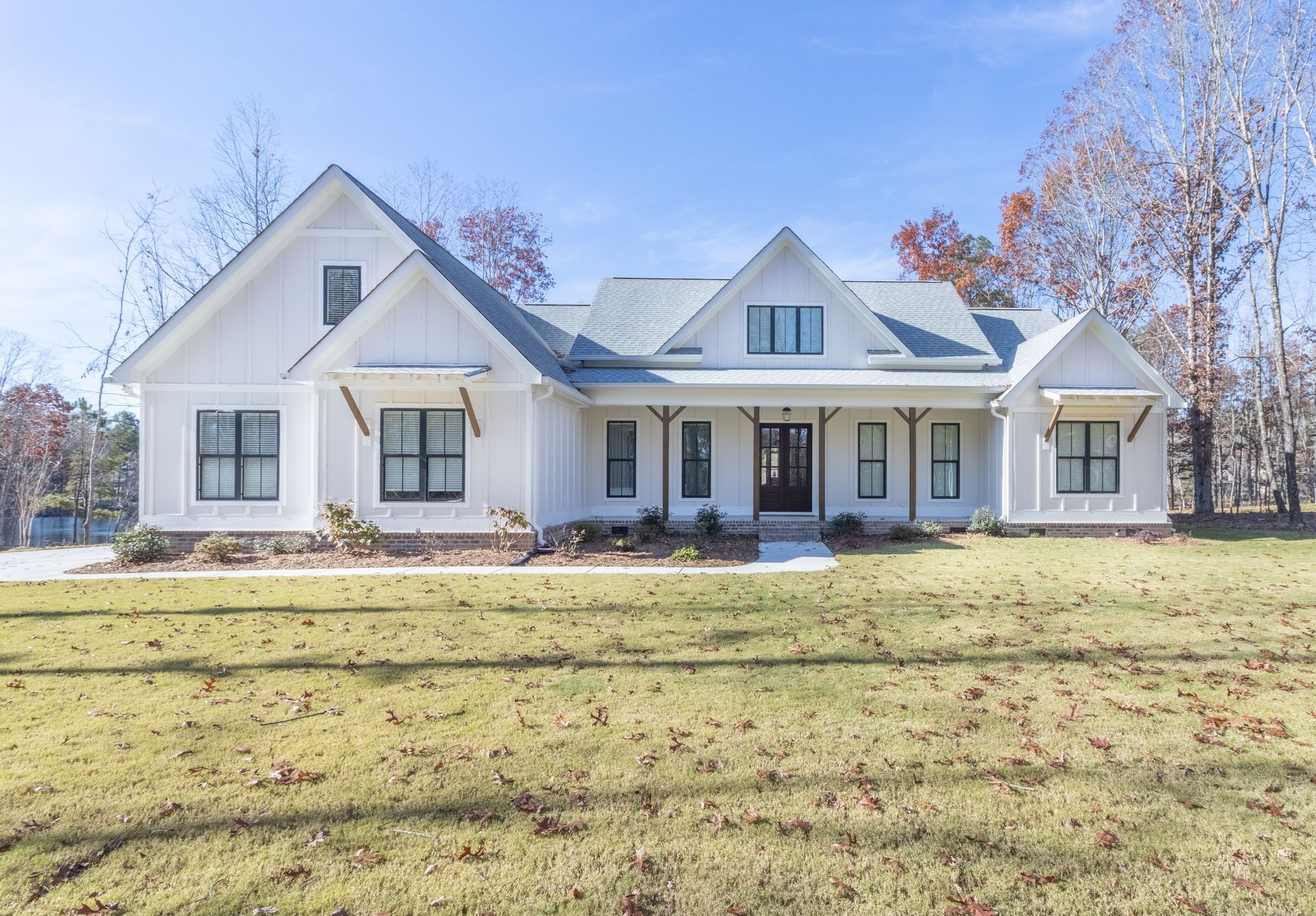 A large white house with black windows is sitting on top of a lush green field.