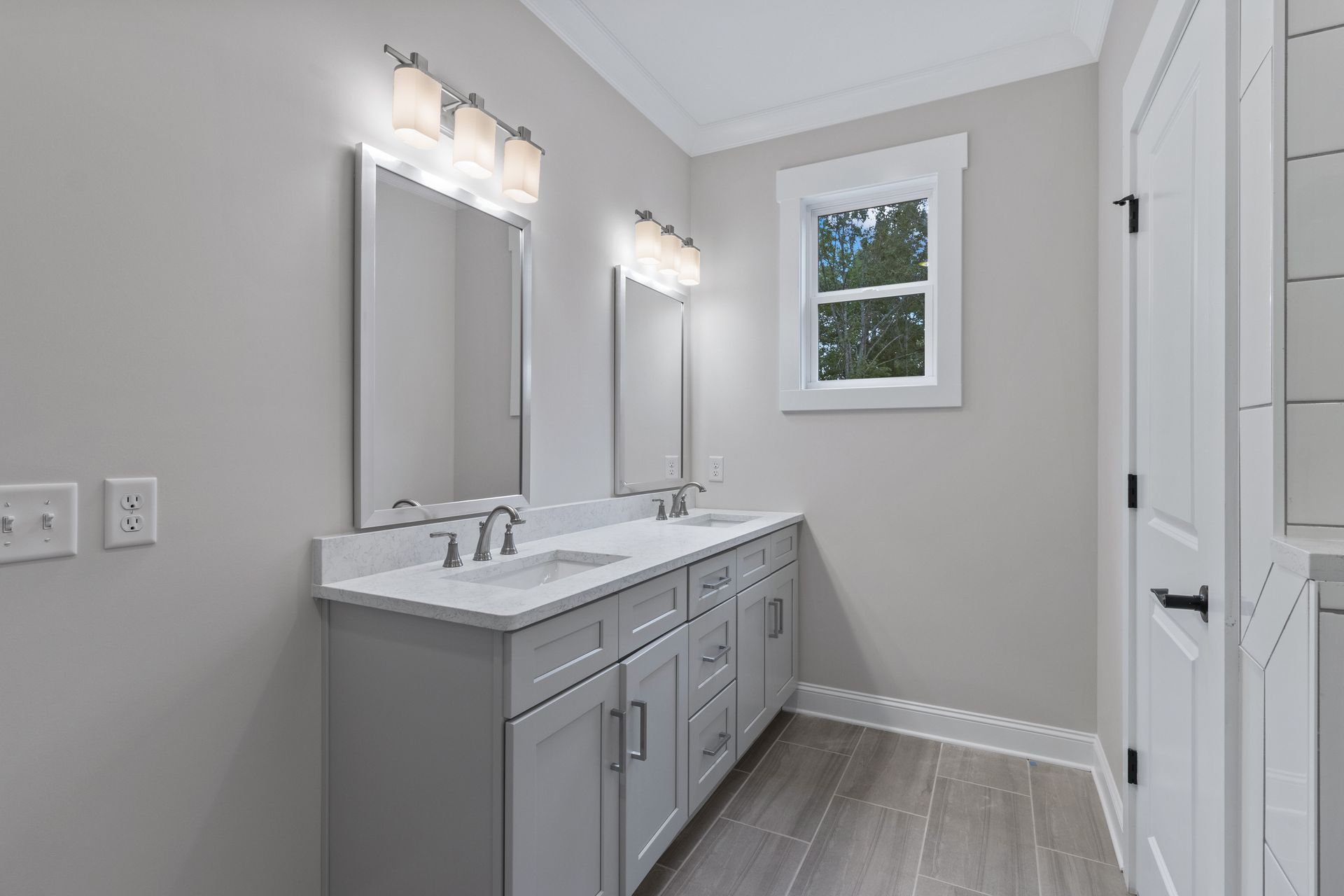 a bathroom with two sinks , two mirrors and a window .