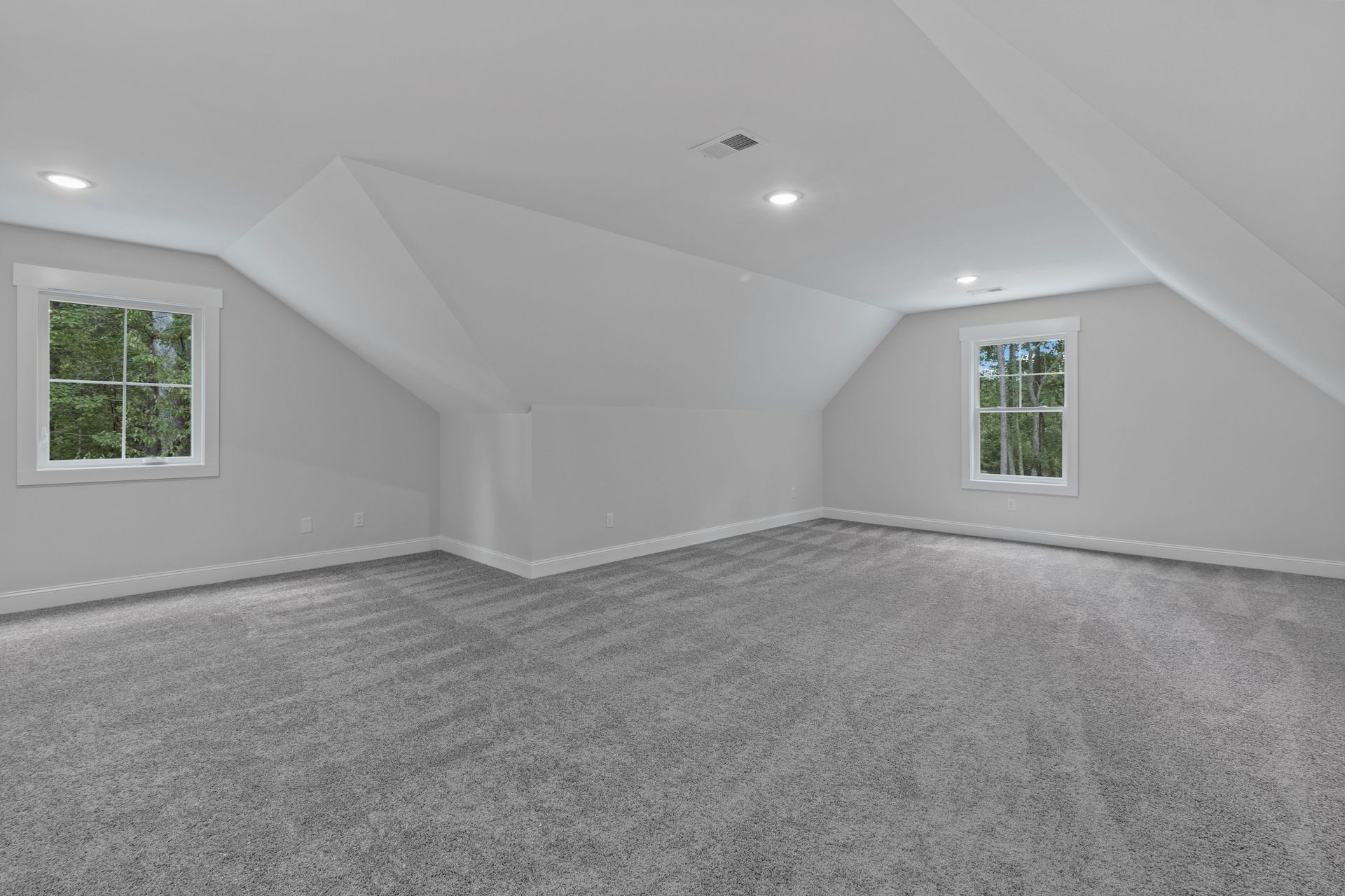 an empty room with a gray carpet and two windows .