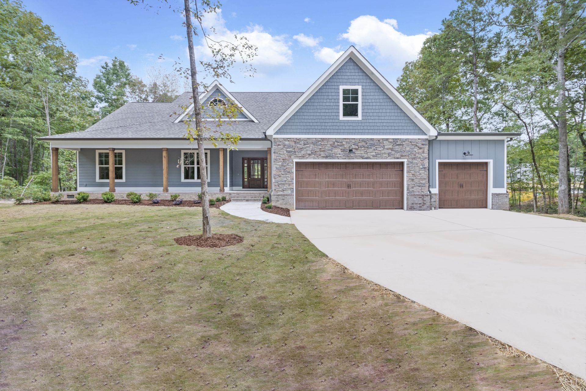 a large blue house with two garages and a driveway surrounded by trees .
