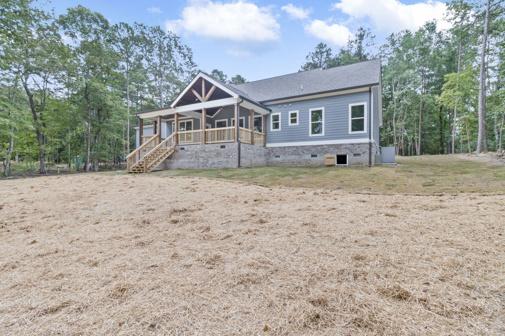 a large house is sitting on top of a dirt field surrounded by trees .