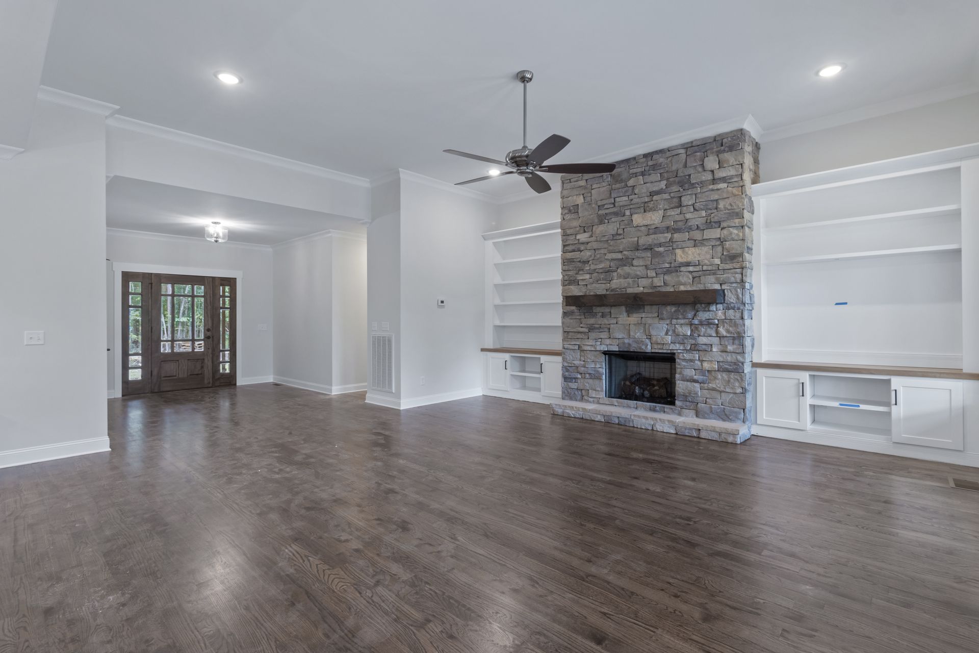 an empty living room with a stone fireplace and a ceiling fan .