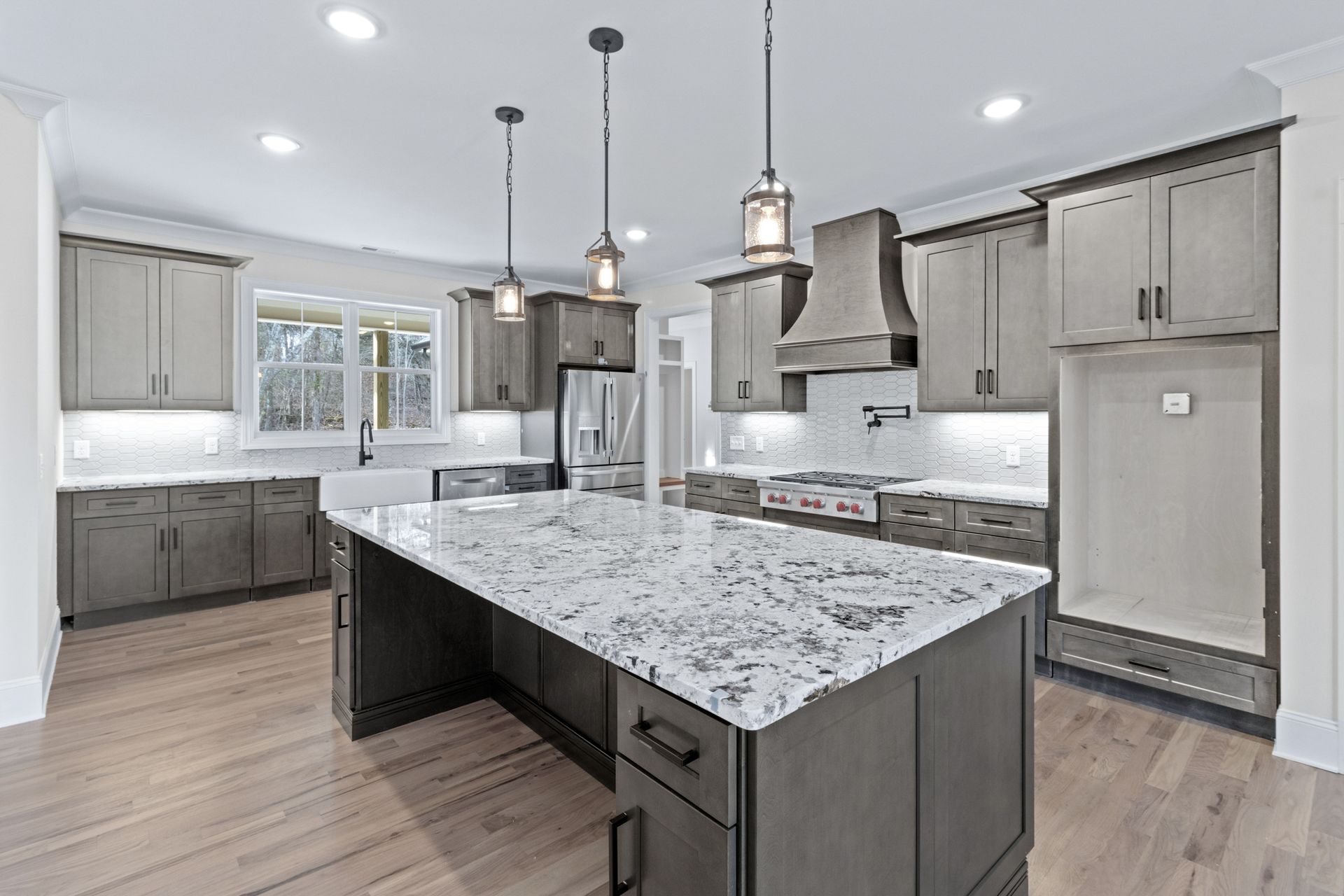 A kitchen with gray cabinets , granite counter tops , and a large island.